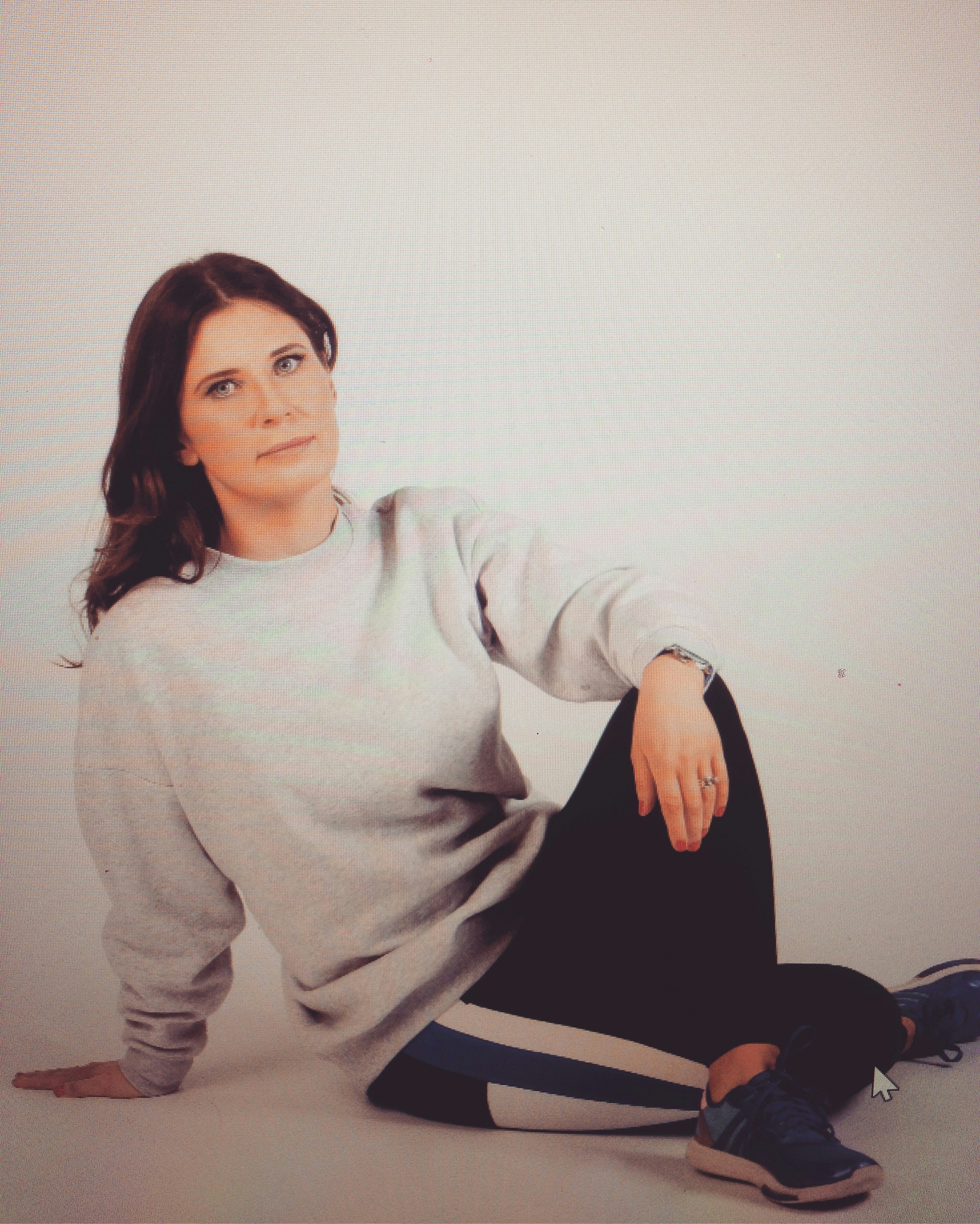 Woman in grey sweatshirt and black pants sitting.
