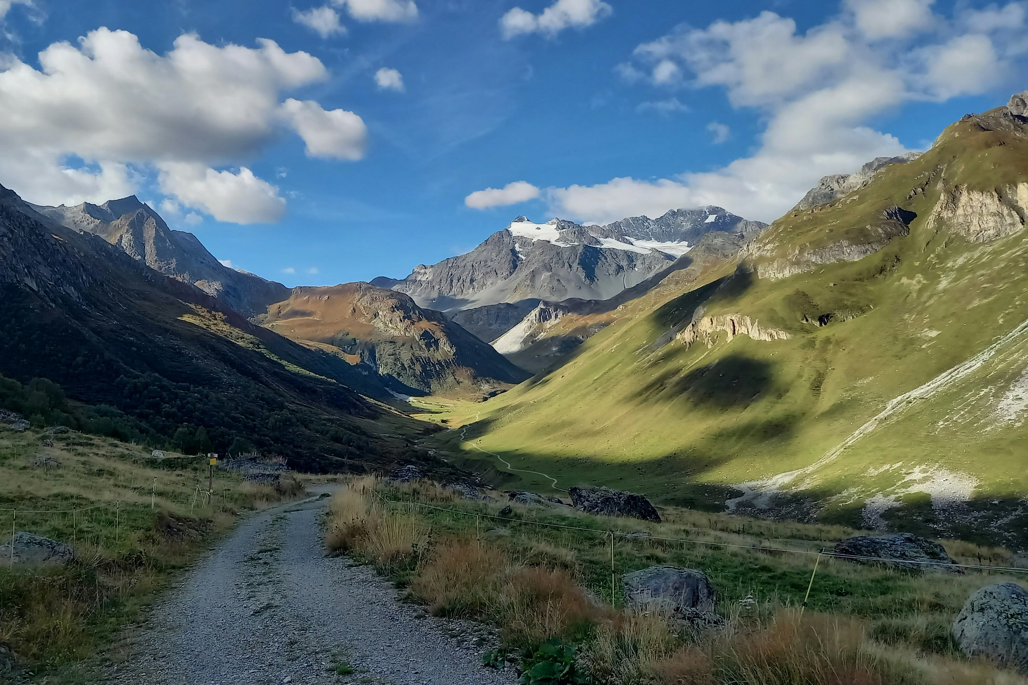 A winding dirt path leads through a green mountain valley.