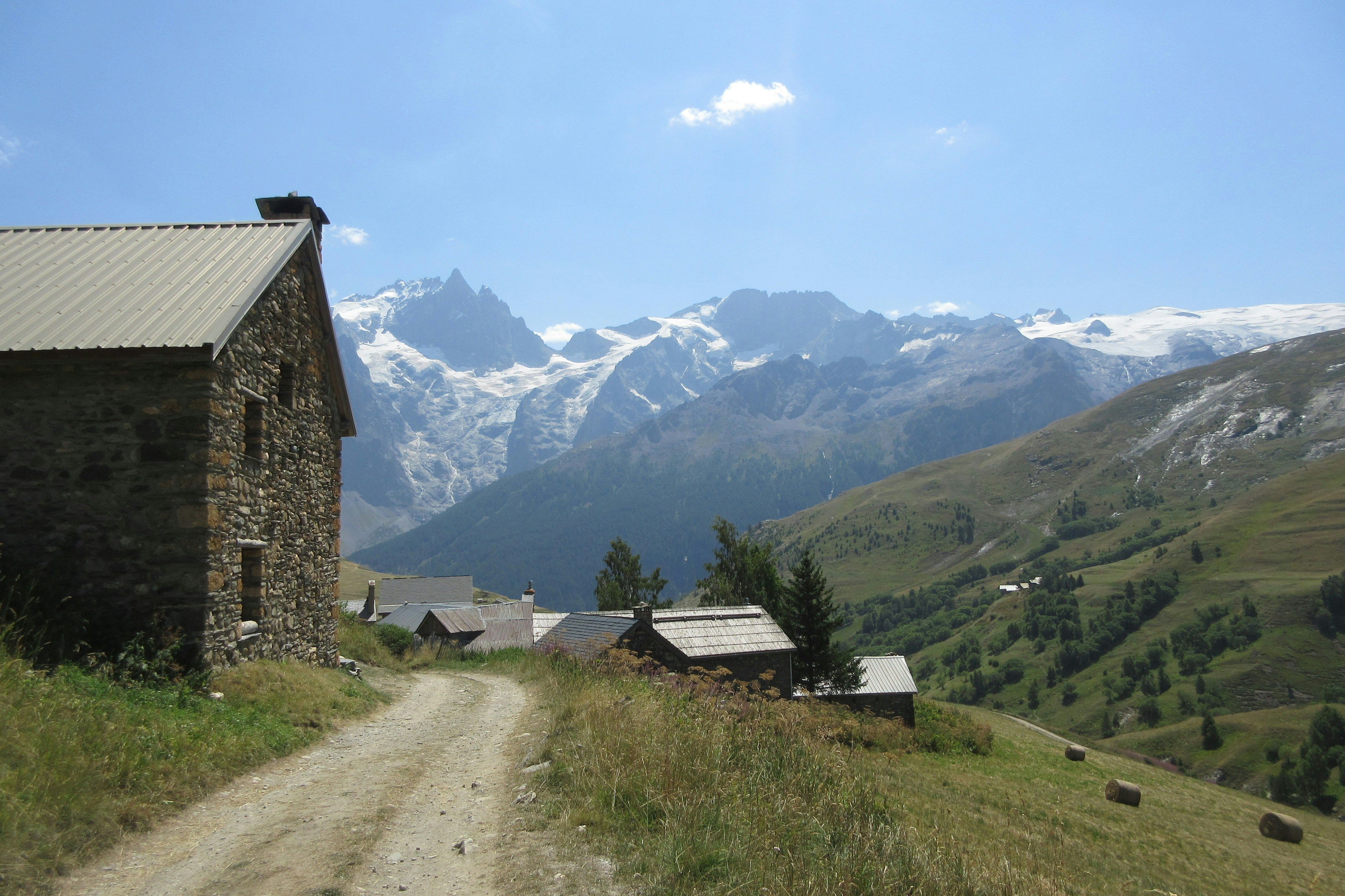 Stone buildings on a mountain path with snowy peaks.