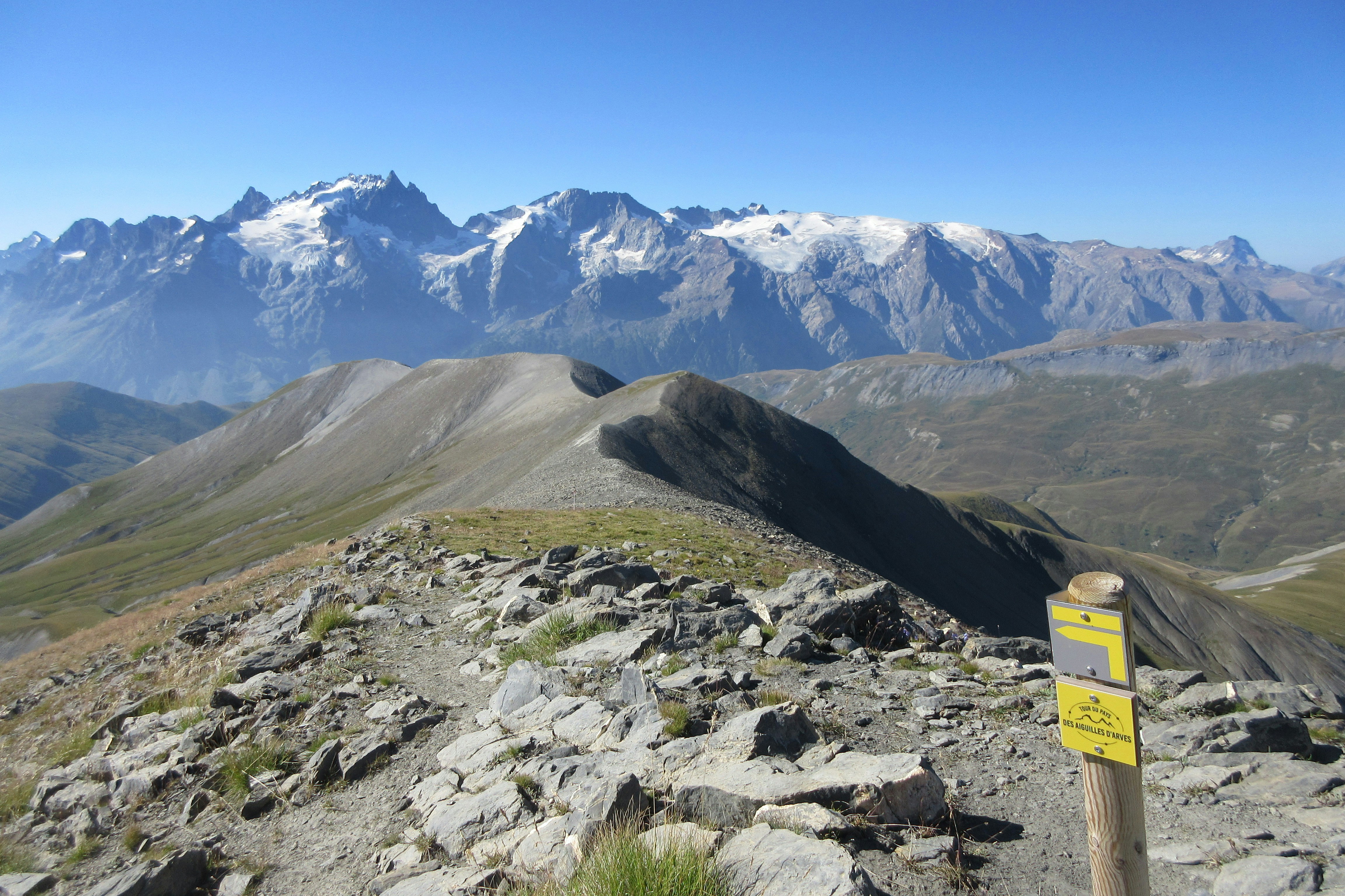 Rocky mountain trail with snow-capped peaks in distance.