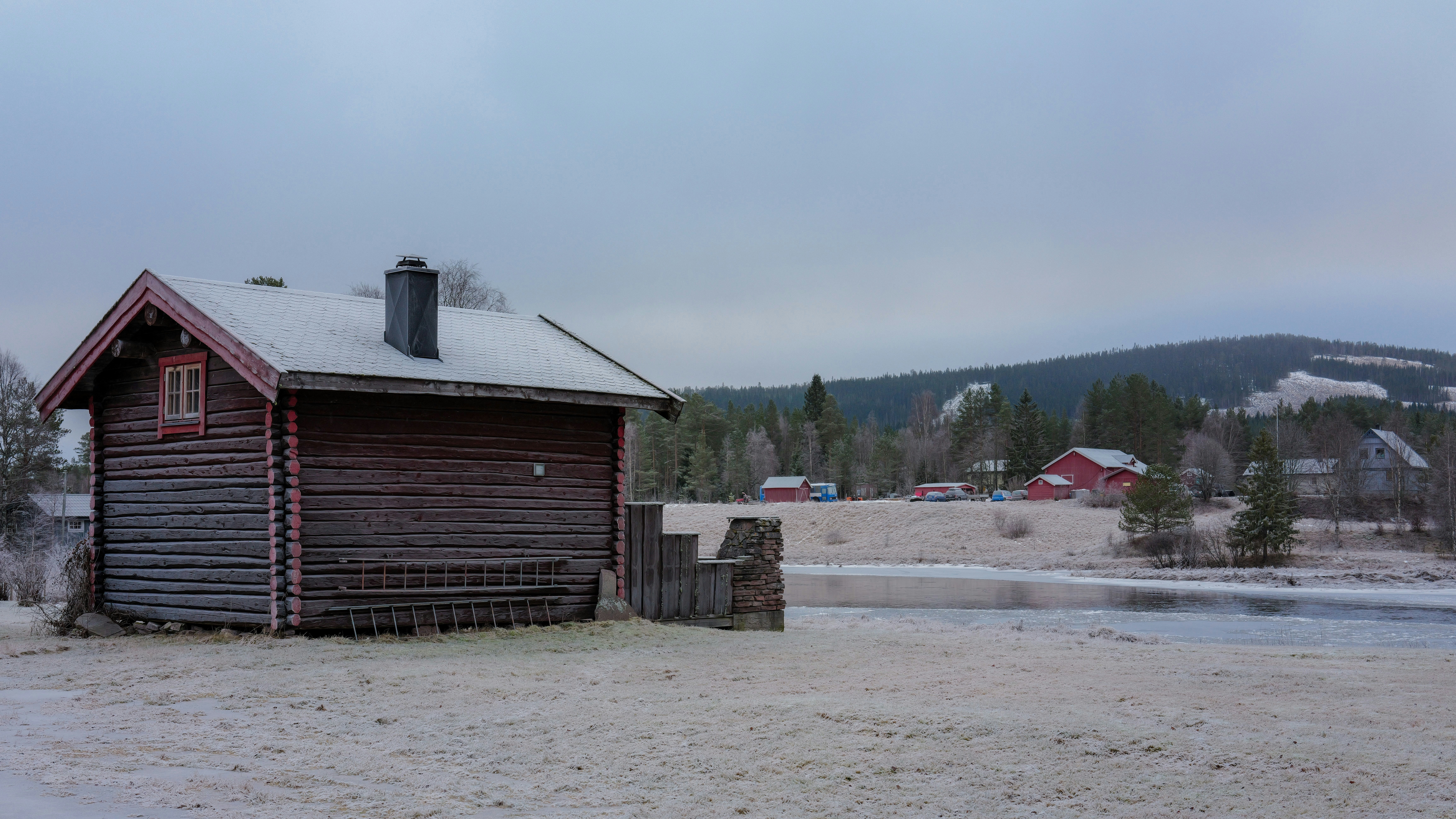Wooden cabin in a snowy landscape with distant houses.