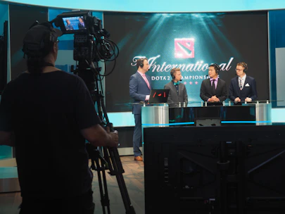 Three men in suits being filmed for dota 2 competition.