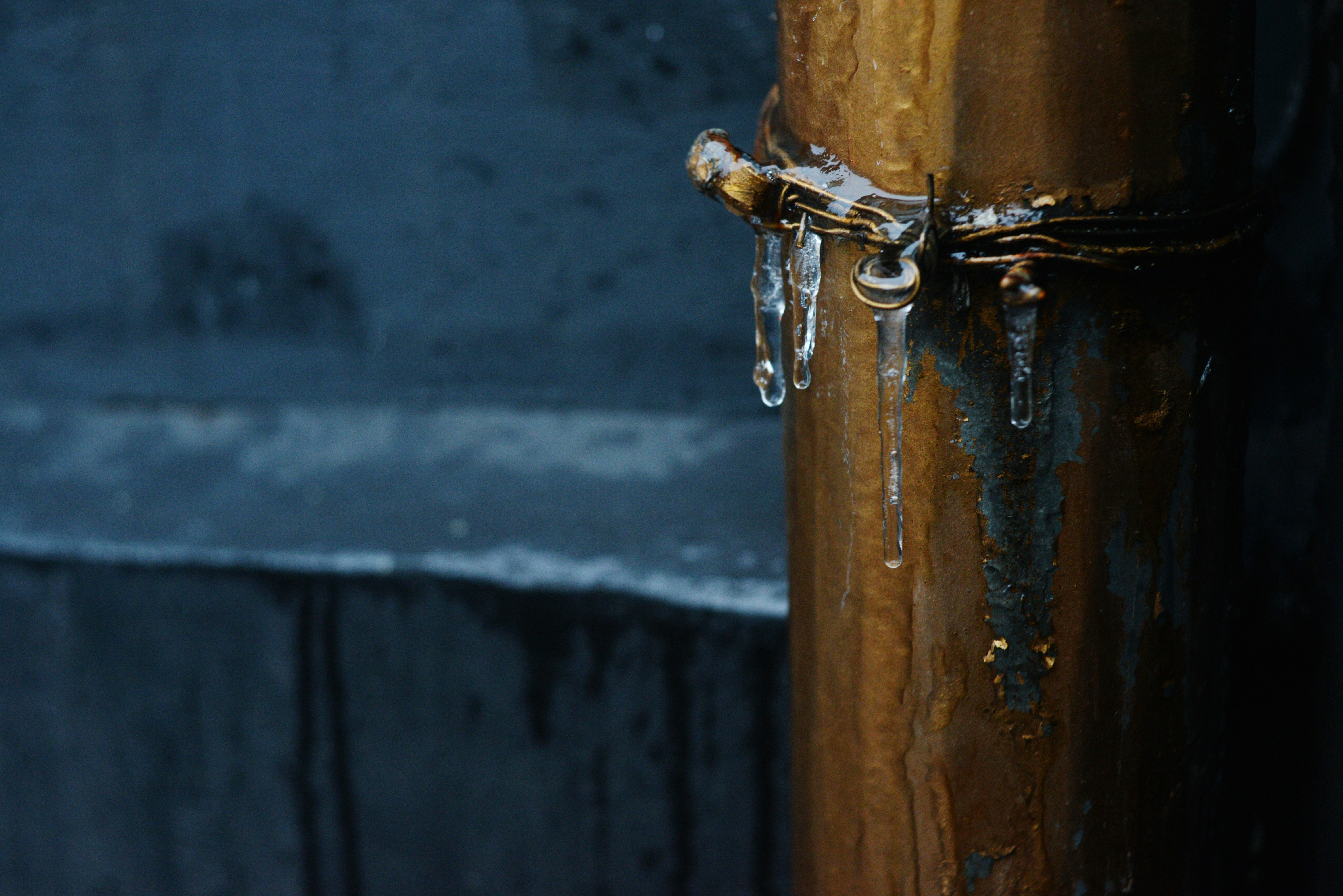 Icicles dripping from a golden pipe outdoors.