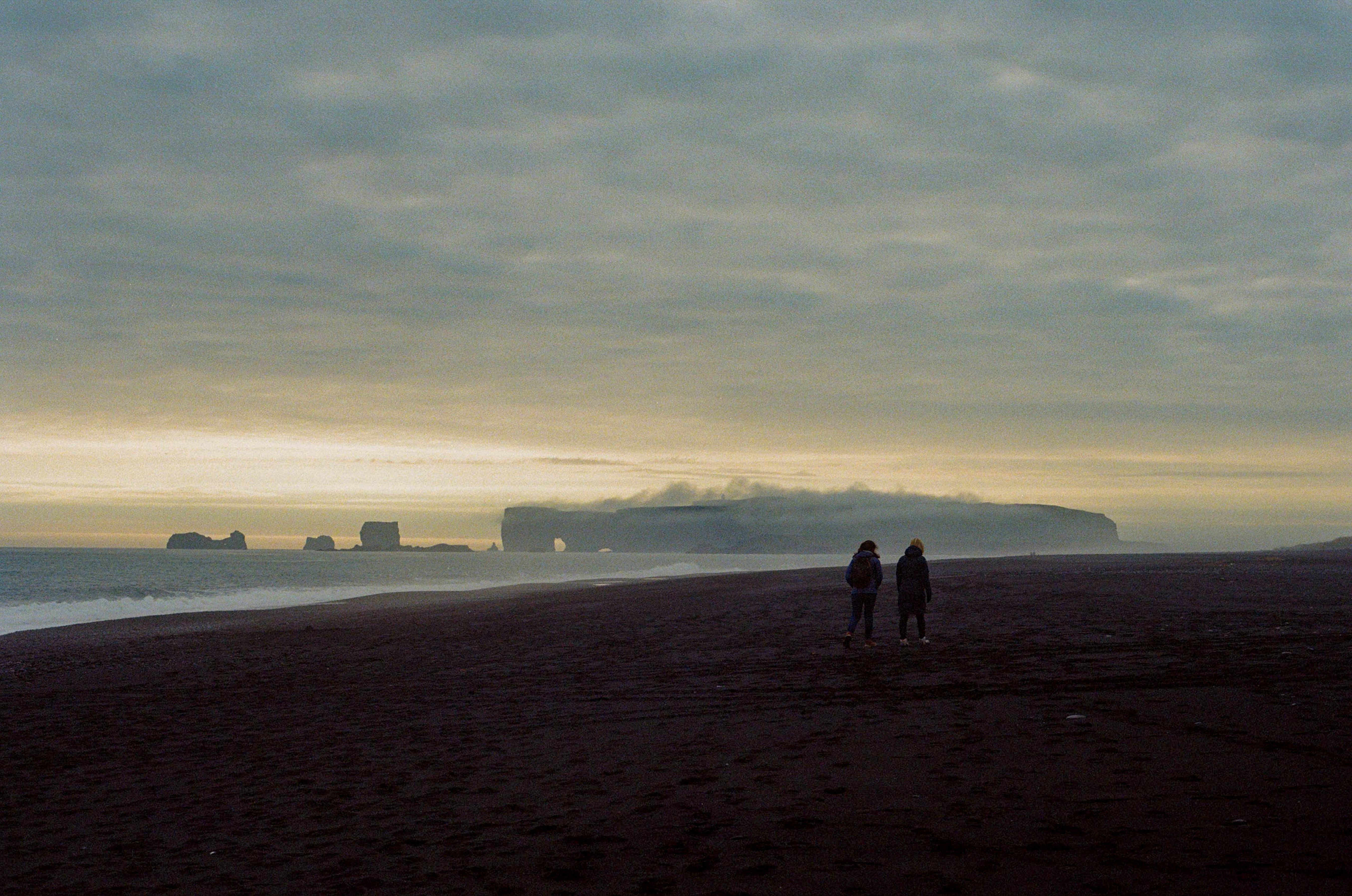 Zwei Personen gehen an einem dunklen Strand mit Meeresnebel.