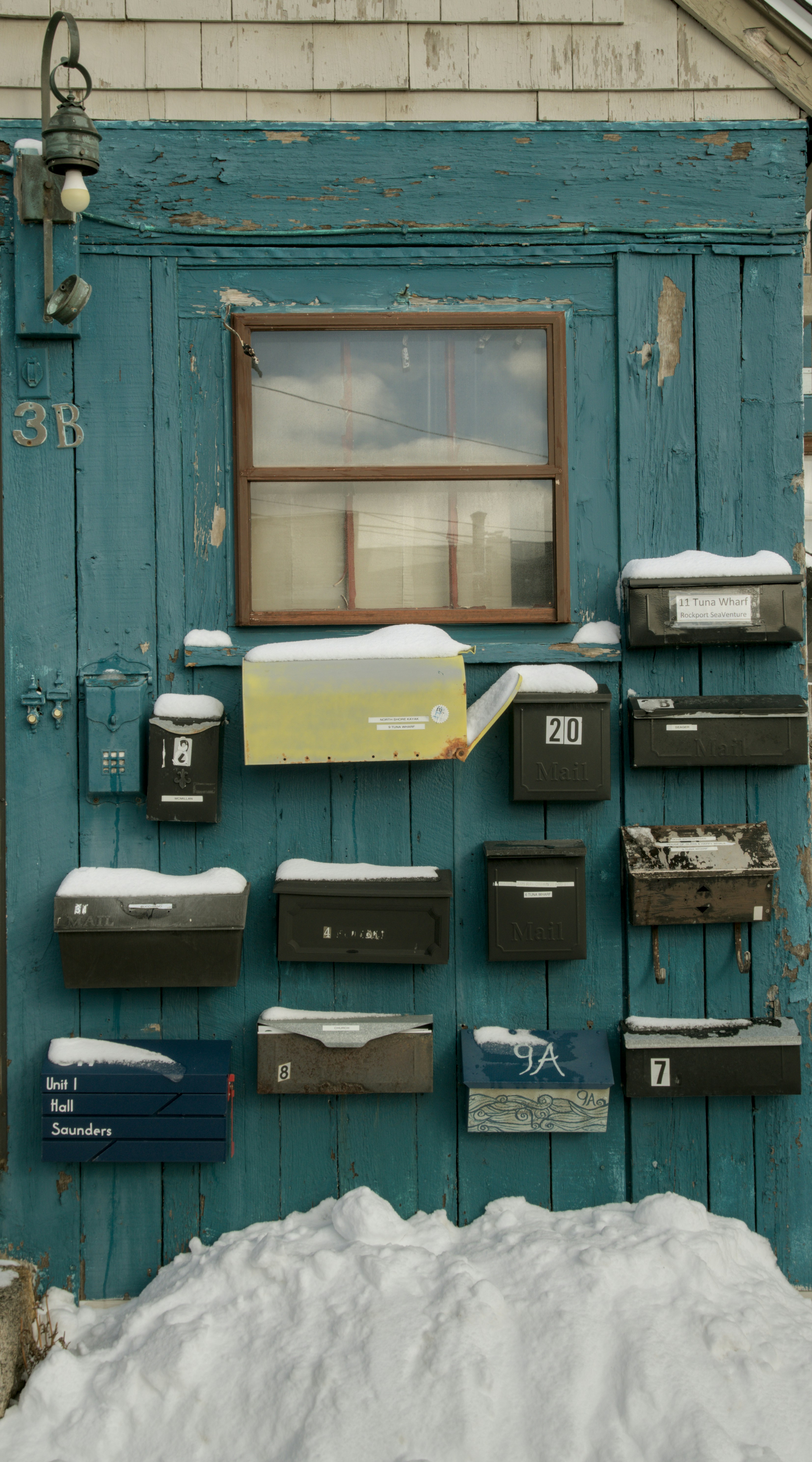 Mailboxes covered in snow on a weathered blue door.