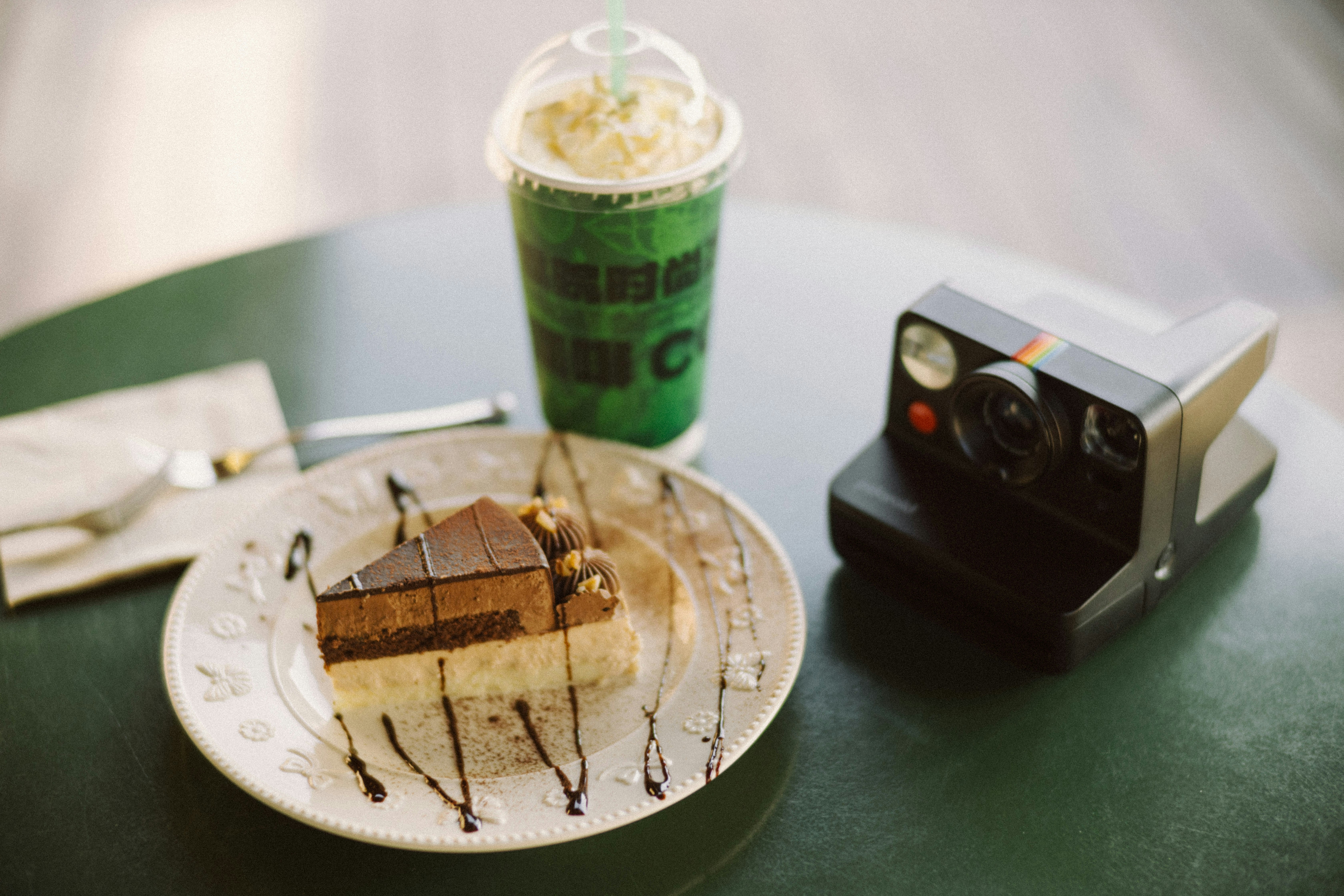 Slice of chocolate cake and green drink with camera