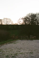 Two empty wooden benches in a gravel courtyard.