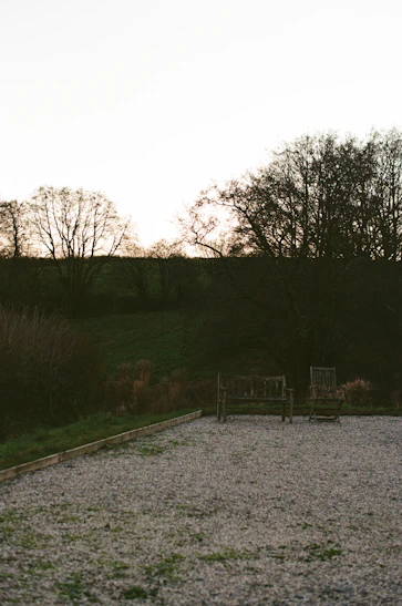 Two empty wooden benches in a gravel courtyard.