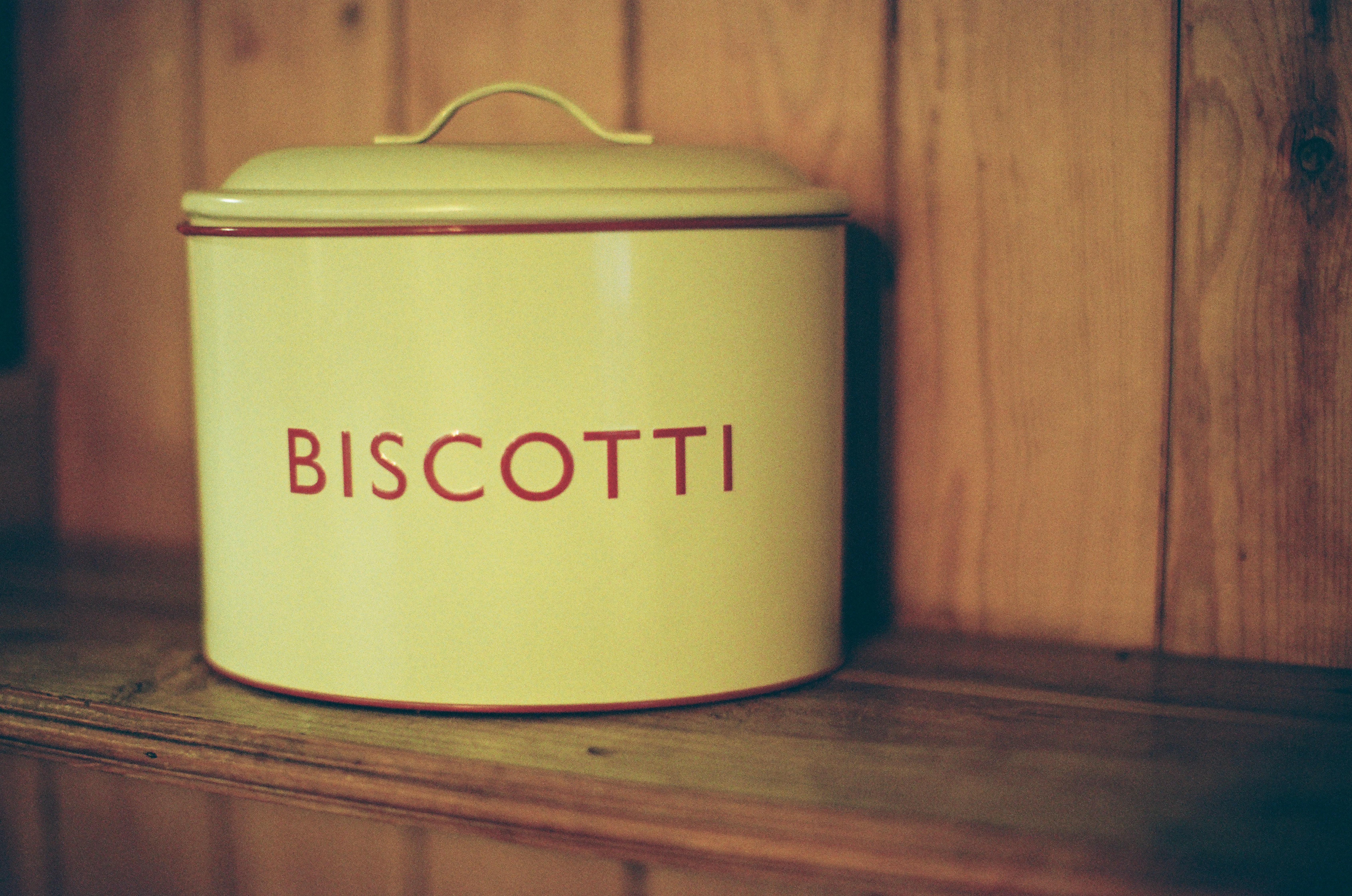 A vintage biscotti tin on a wooden shelf.