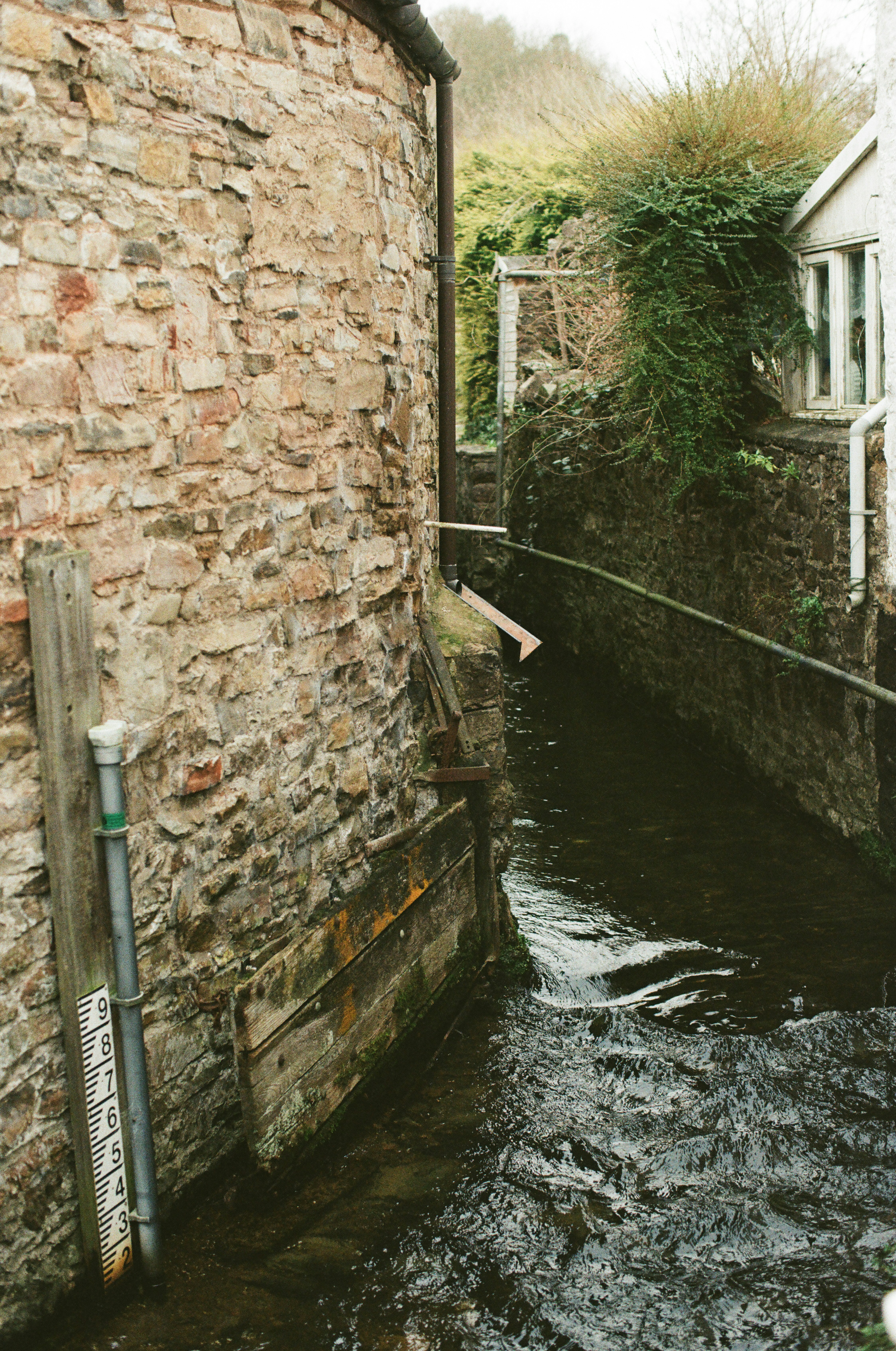 Un ruscello stretto scorre tra muri di pietra e edifici.