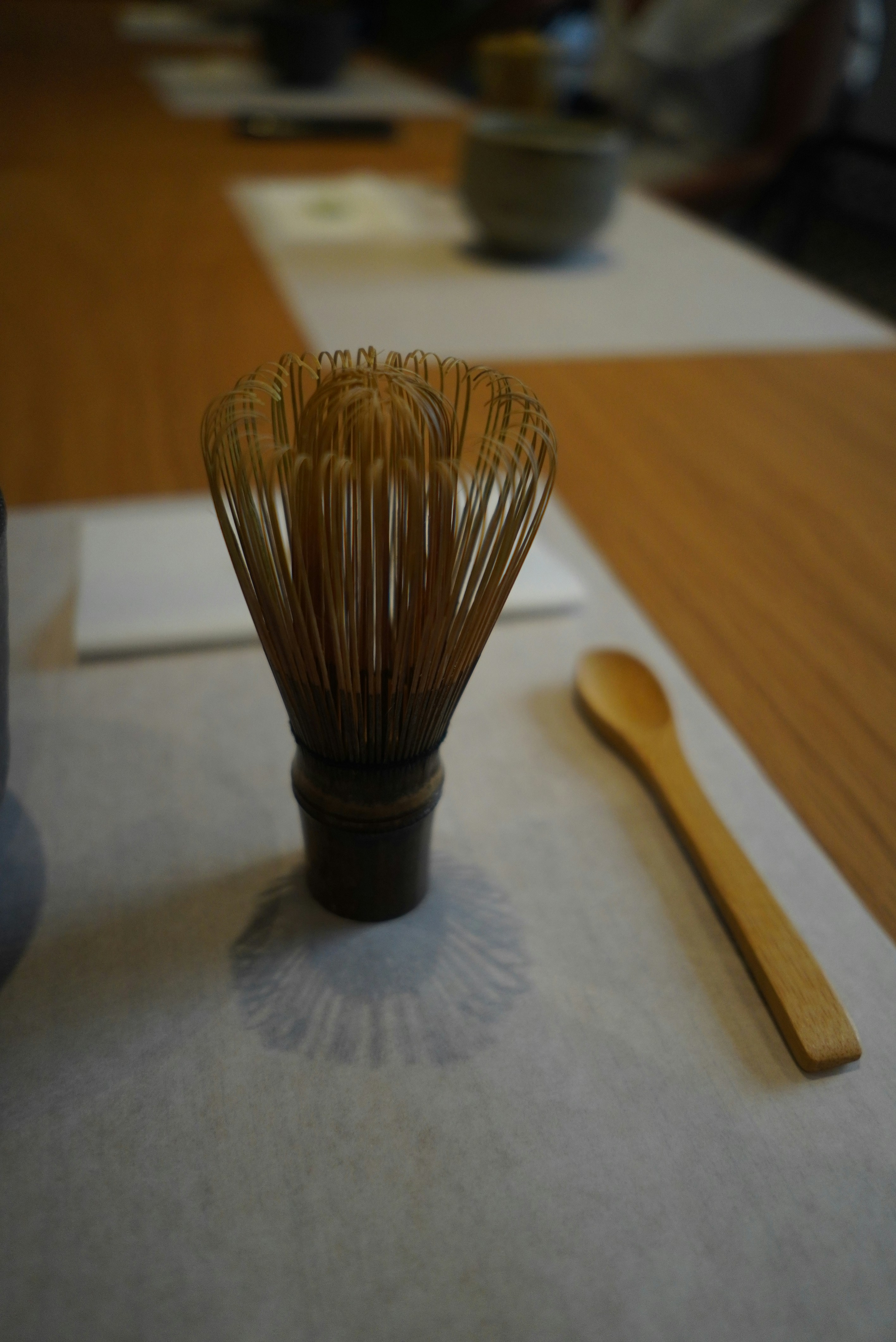 A bamboo whisk and wooden spoon on a table.