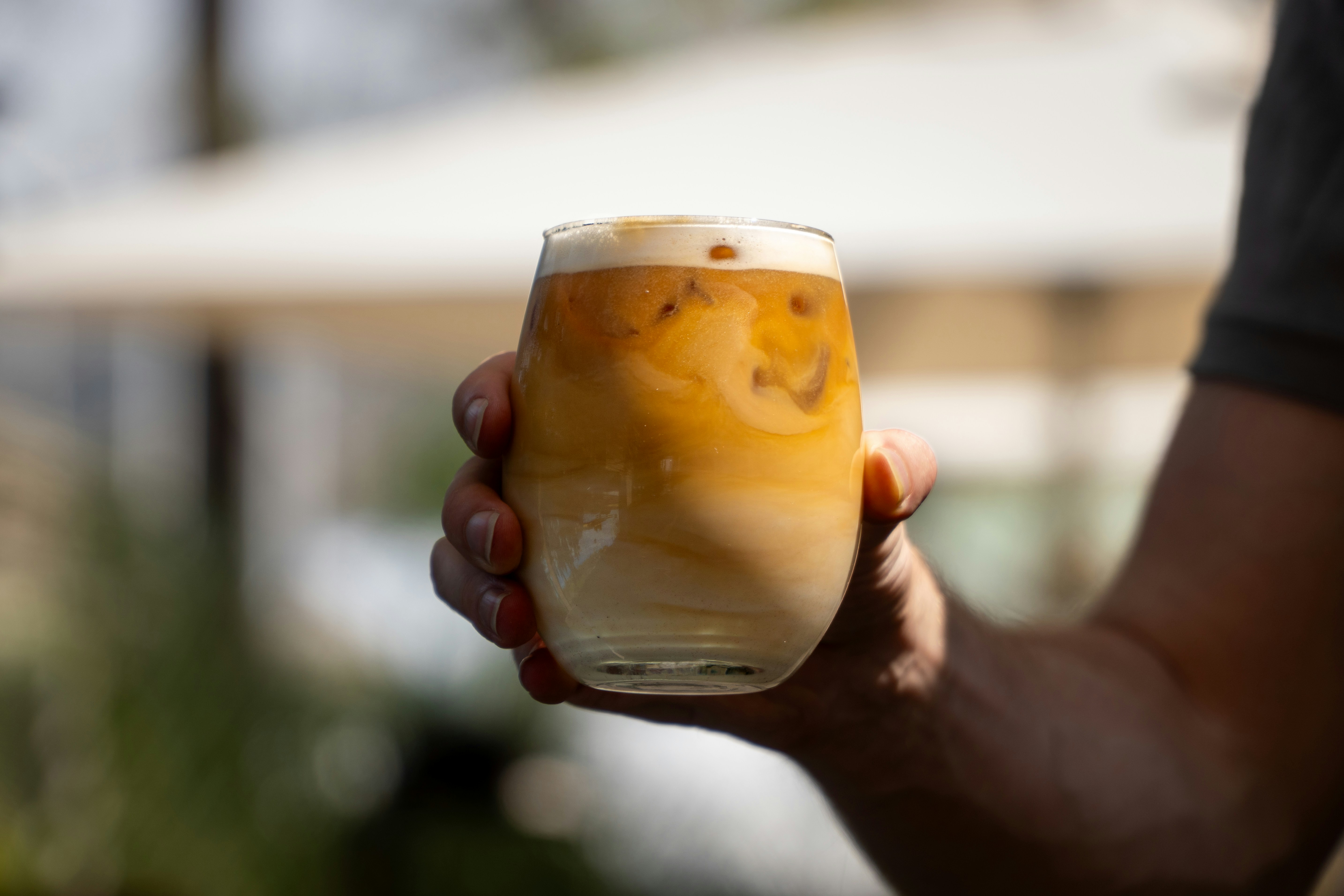 Hand holding a glass of iced coffee with cream