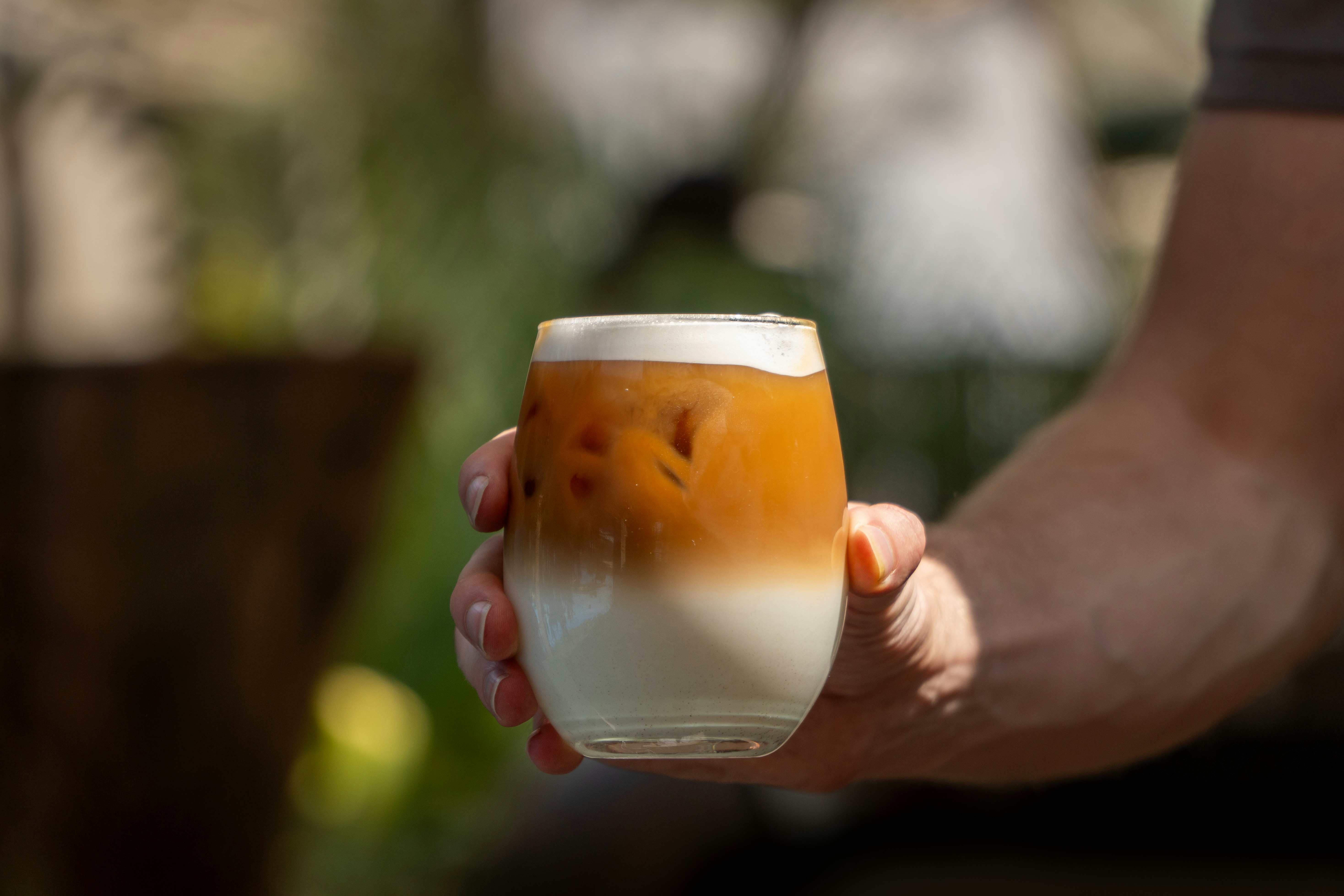 Hand holding a layered iced coffee with foam