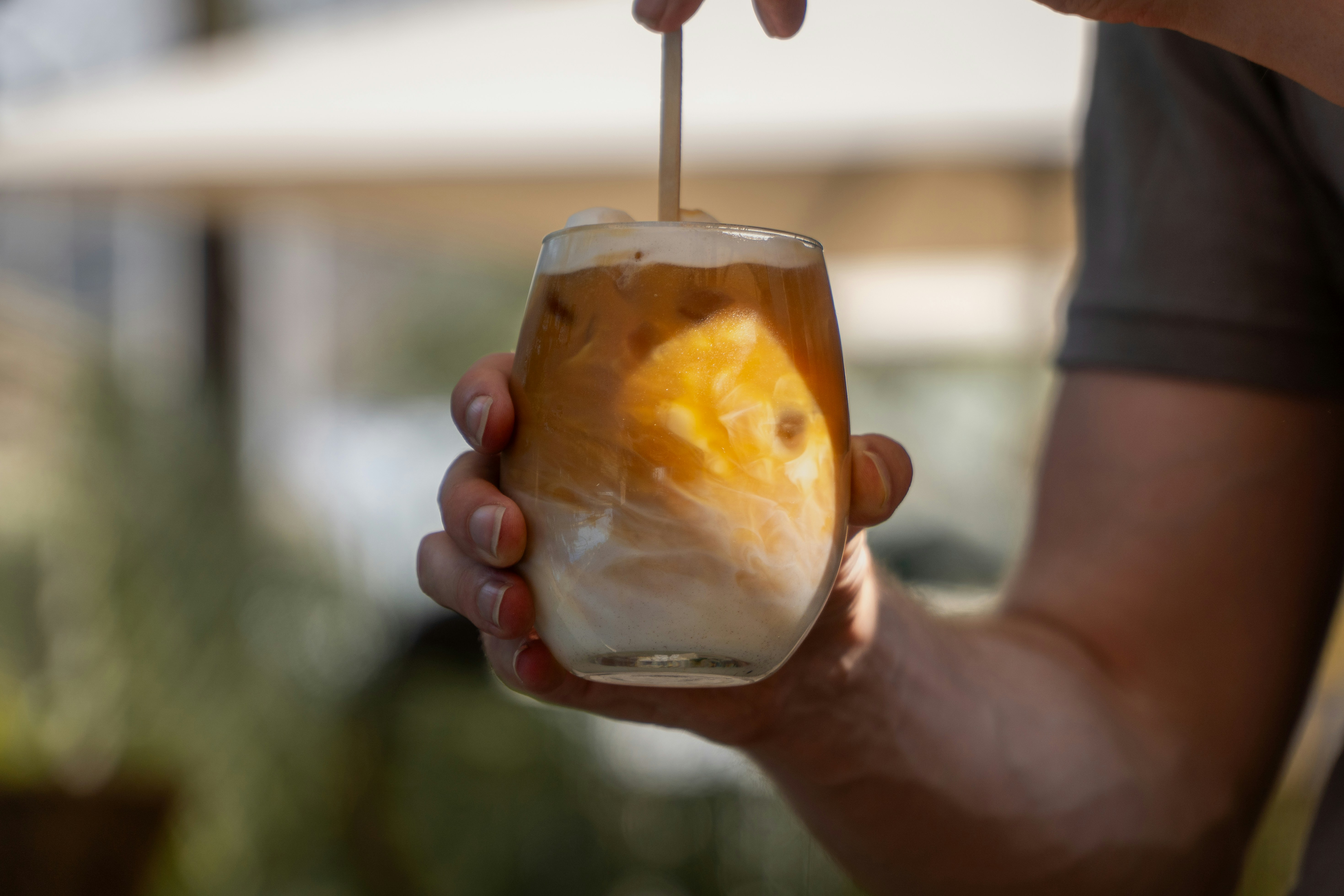 A person holds a glass of iced coffee with cream.