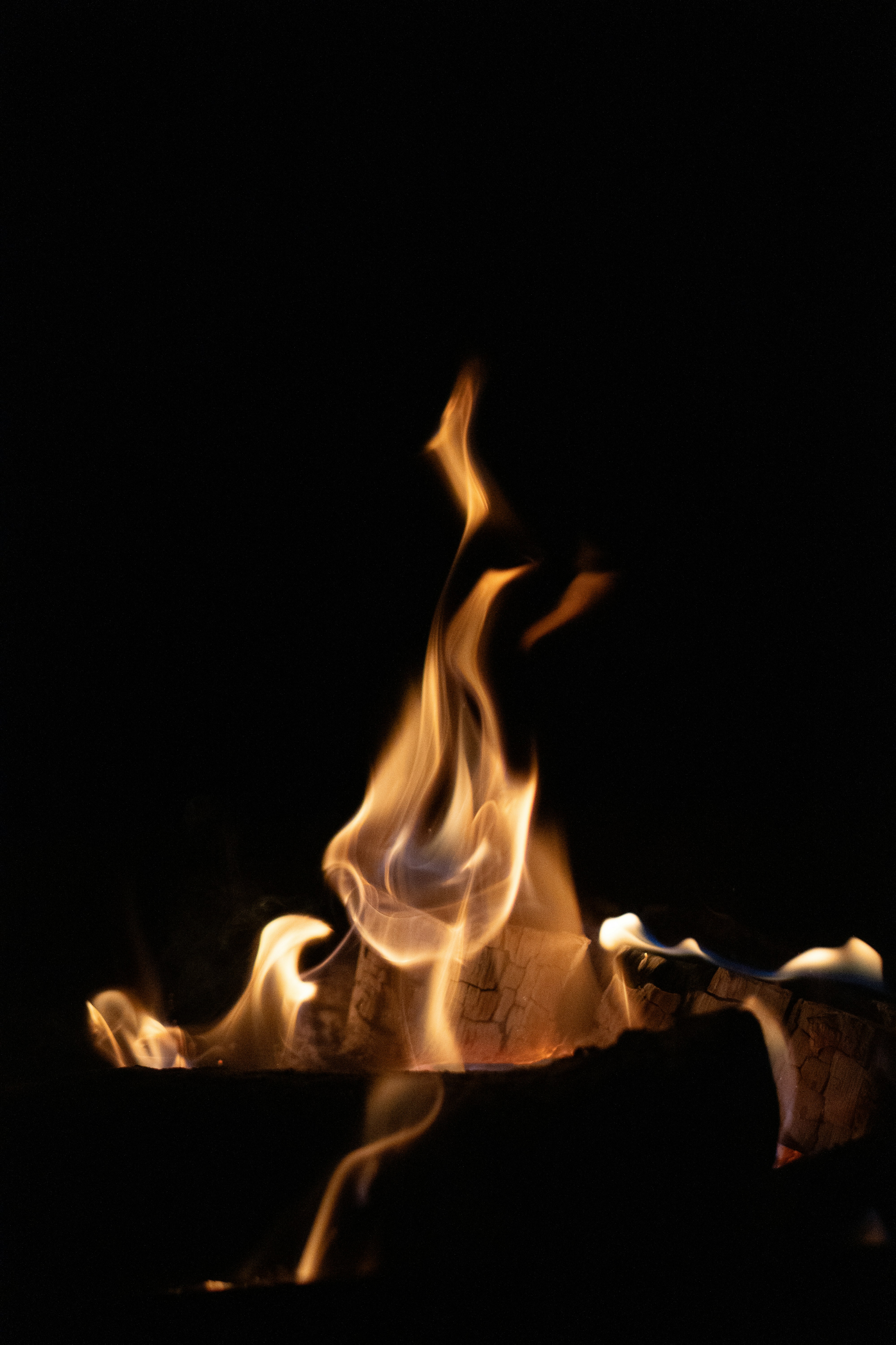Flames dance on burning logs in darkness.