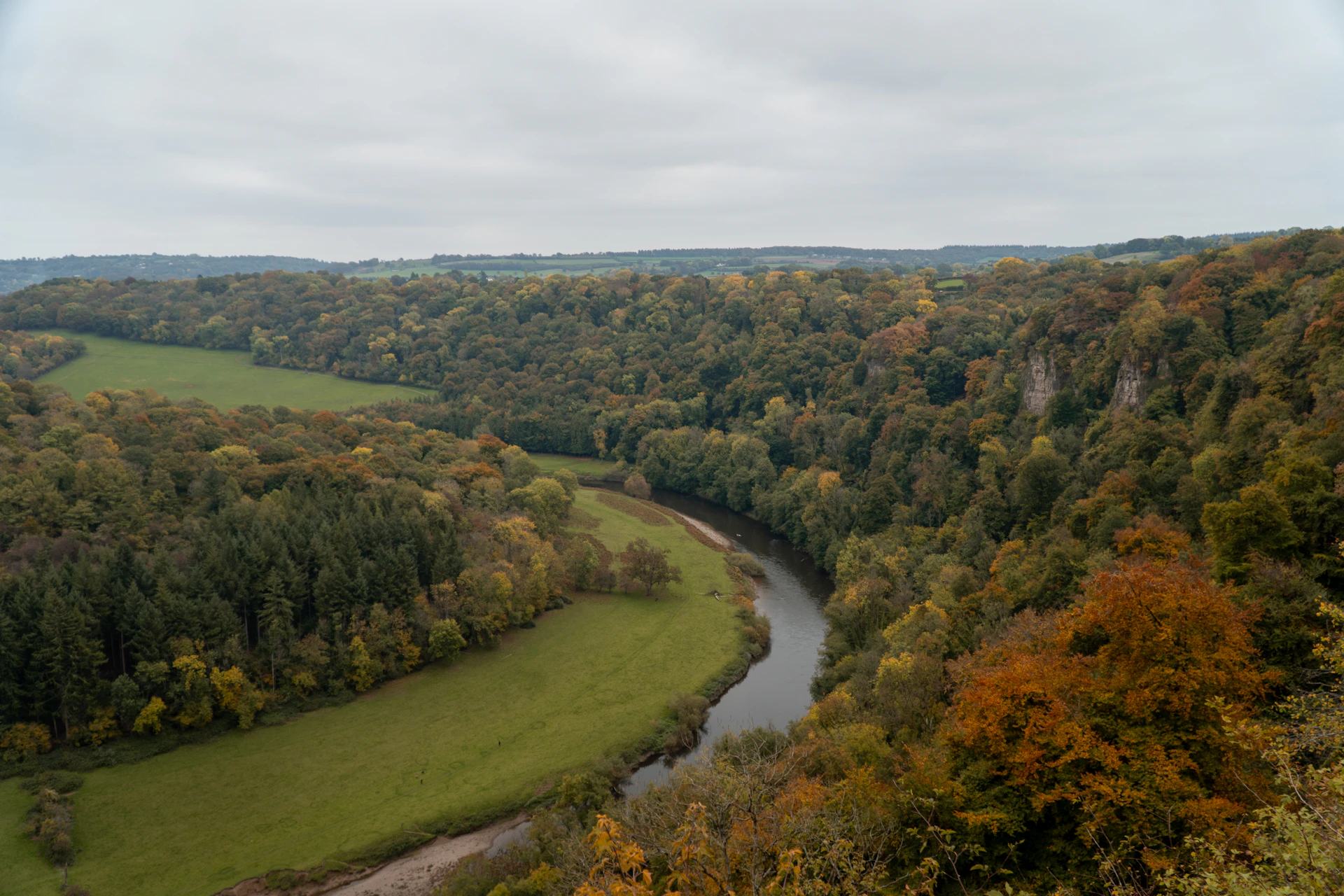 A winding river flows through a forested valley in autumn.