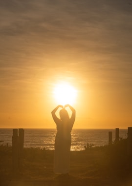Silhouette of a person making a heart shape at sunset.