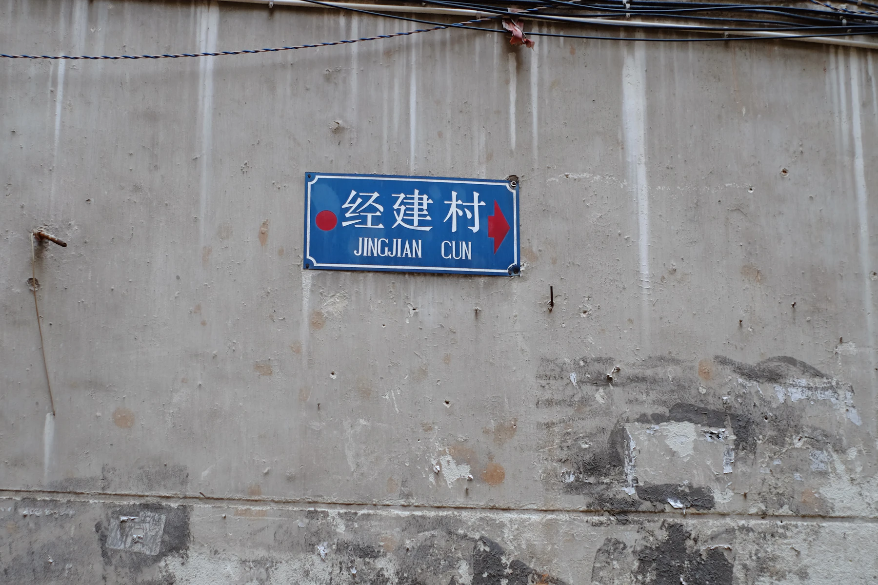 A blue enamel street plate on a weathered concrete wall, three white Chinese characters above their pinyin spelling