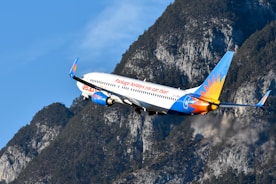 Airplane flying past a mountain under a blue sky.