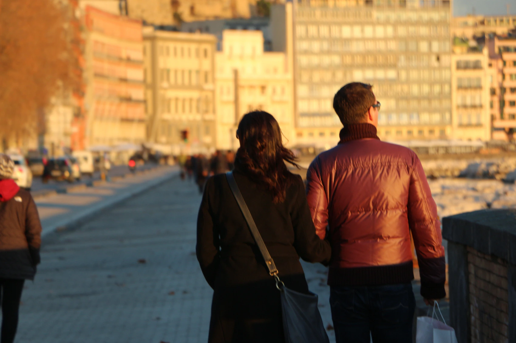 A couple walking along the Naples waterfront in warm winter light