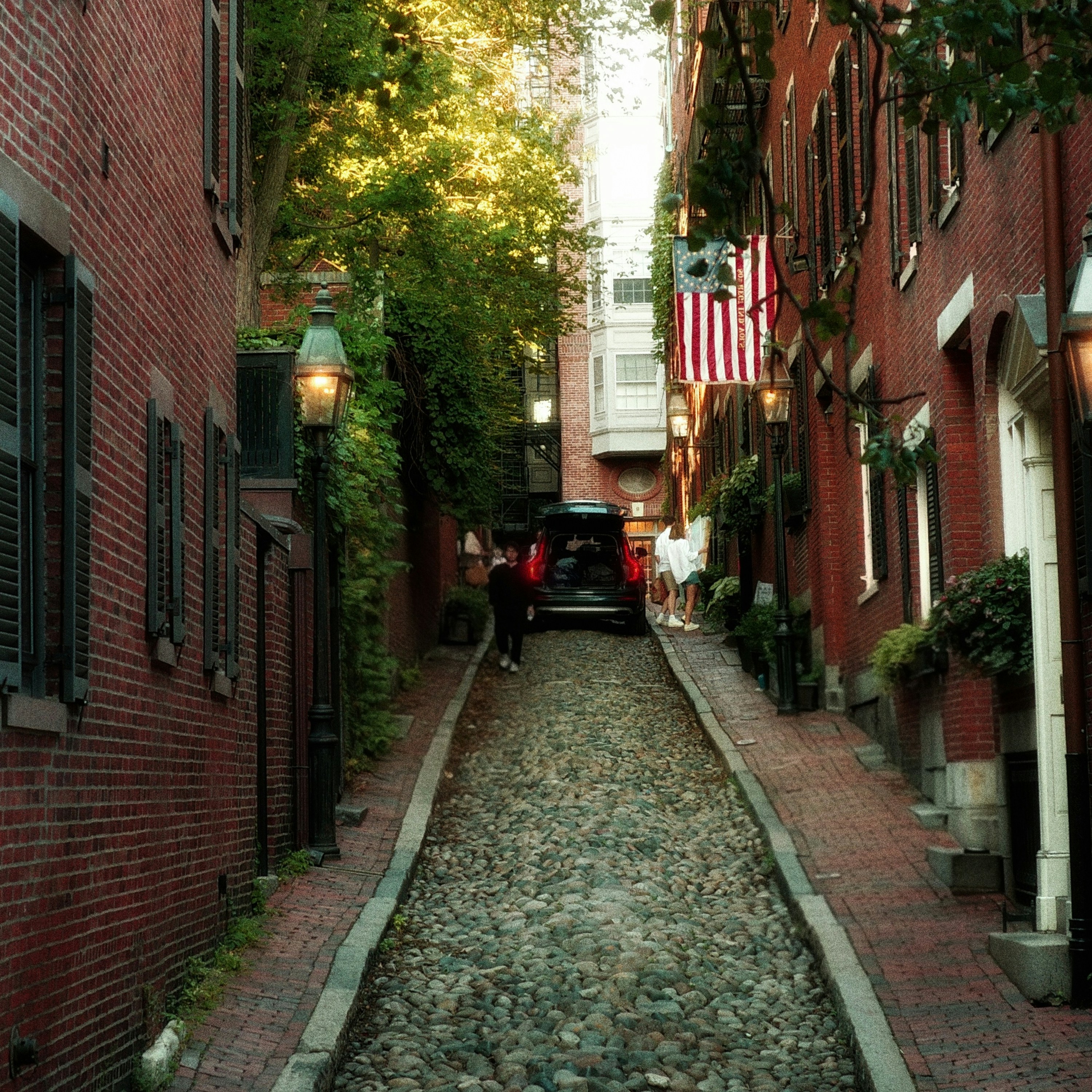 Cobblestone street lined with brick buildings and trees.