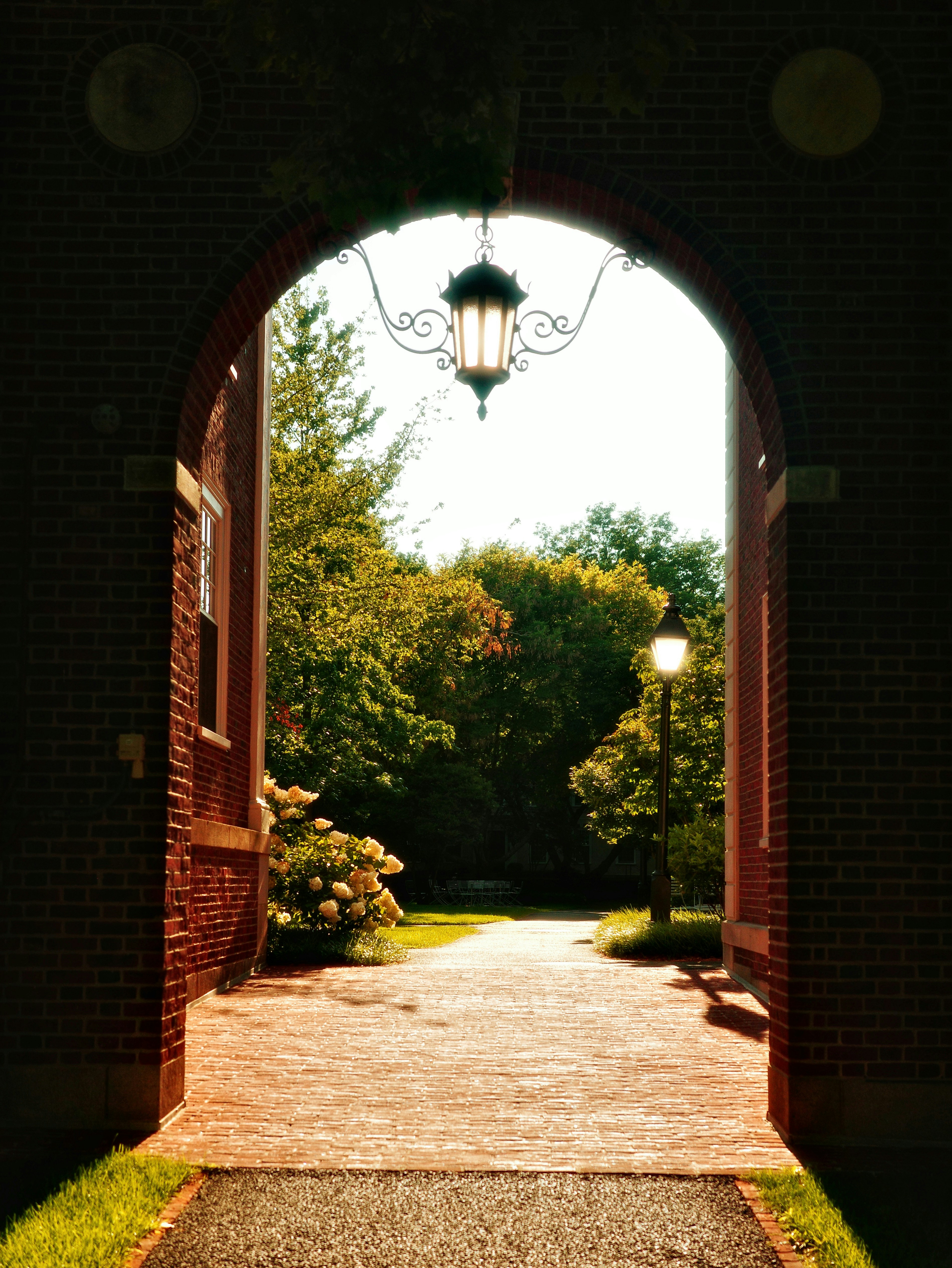 Arched brick entryway leading to a sunlit garden path