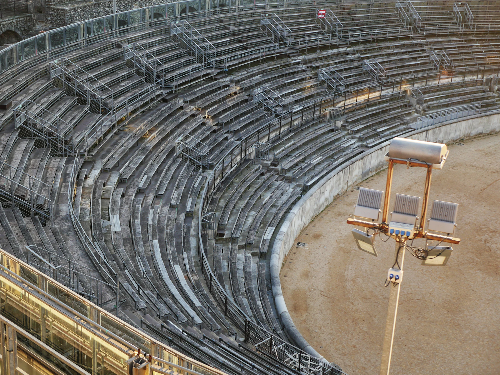Sweeping rows of empty stadium seating with a floodlight fixture in the foreground