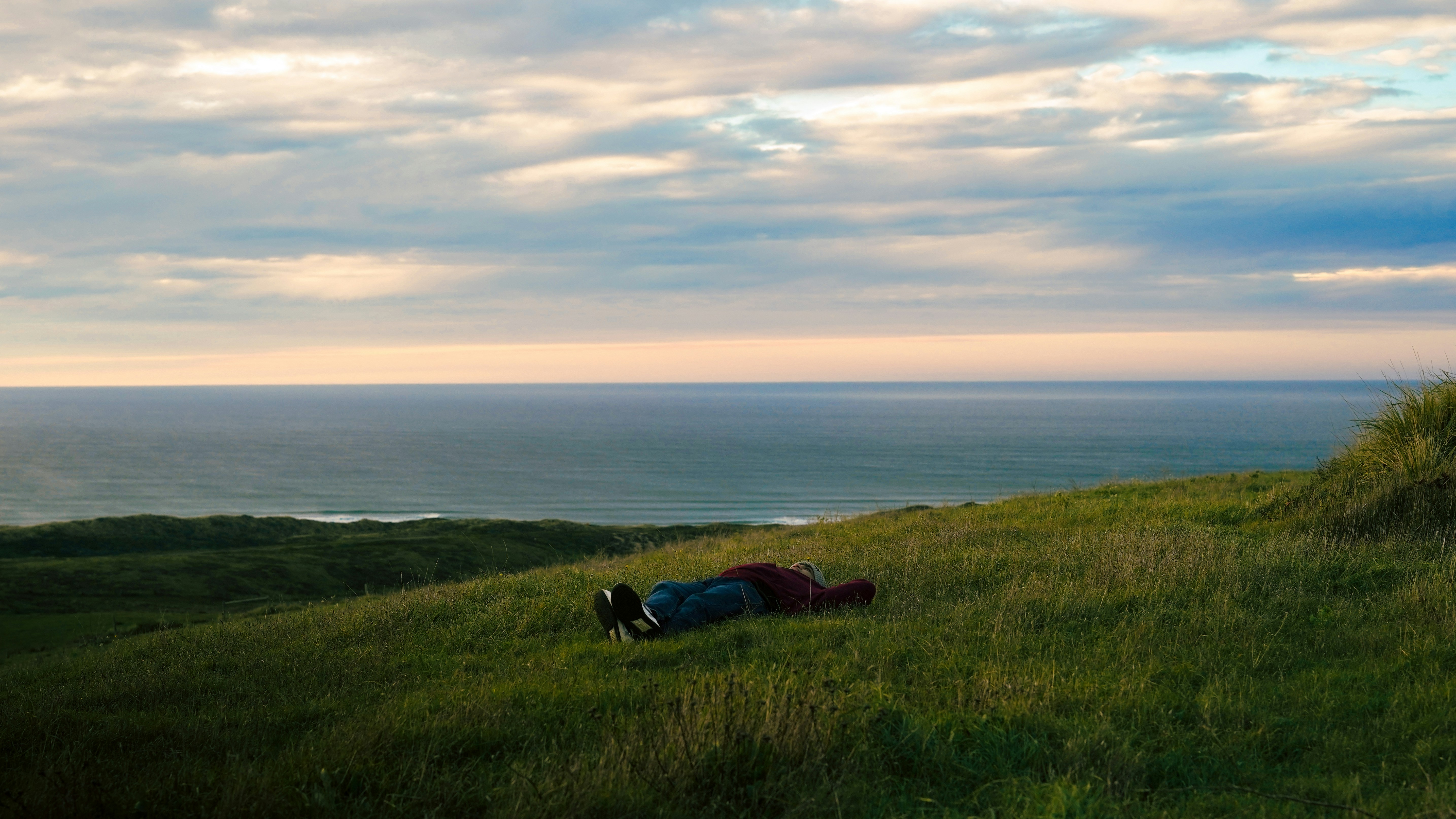 Eine Person liegt auf einem grasbewachsenen Hügel mit Blick auf den Ozean.