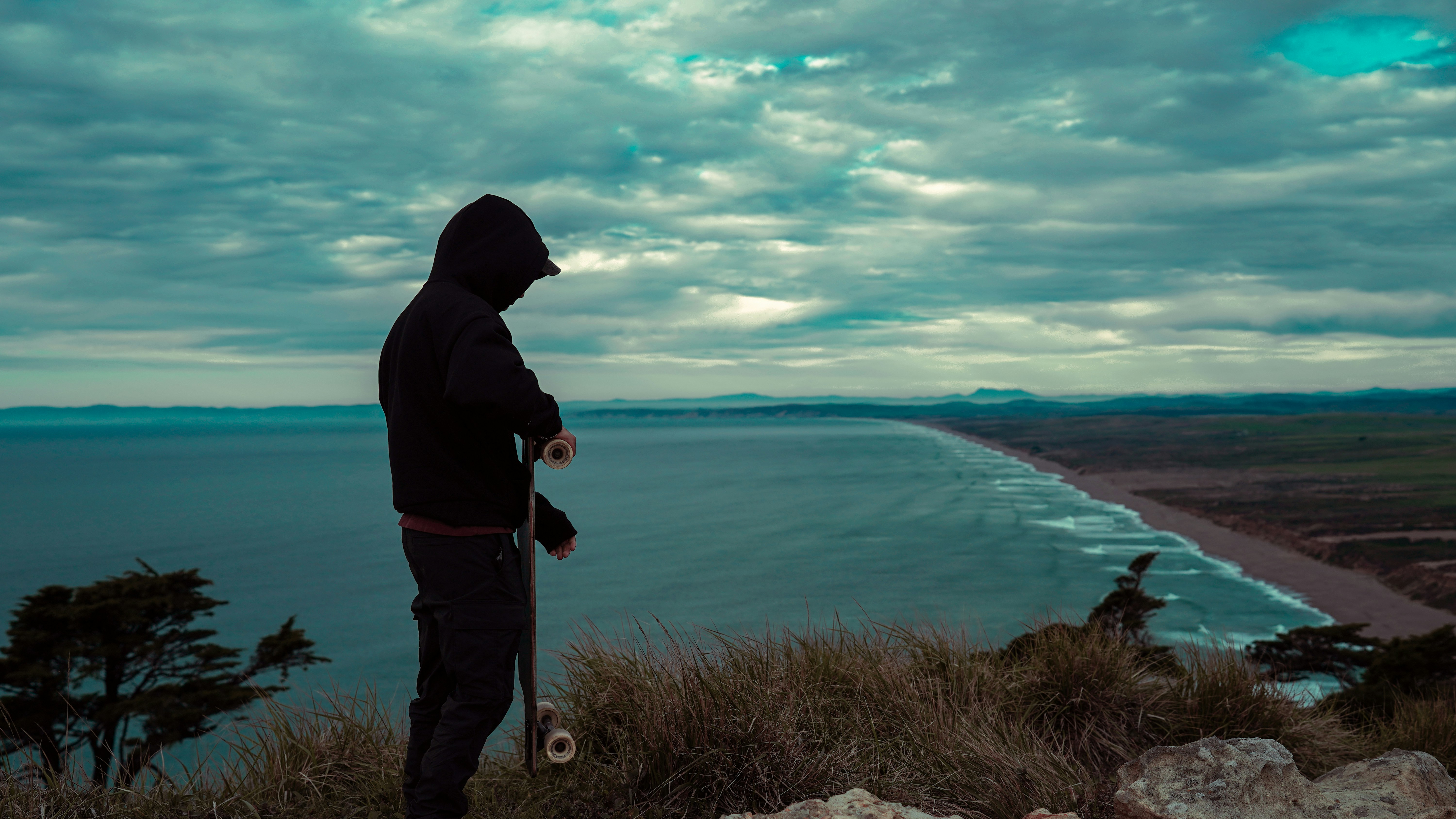 Person mit Skateboard mit Blick auf Ozean und Küste.