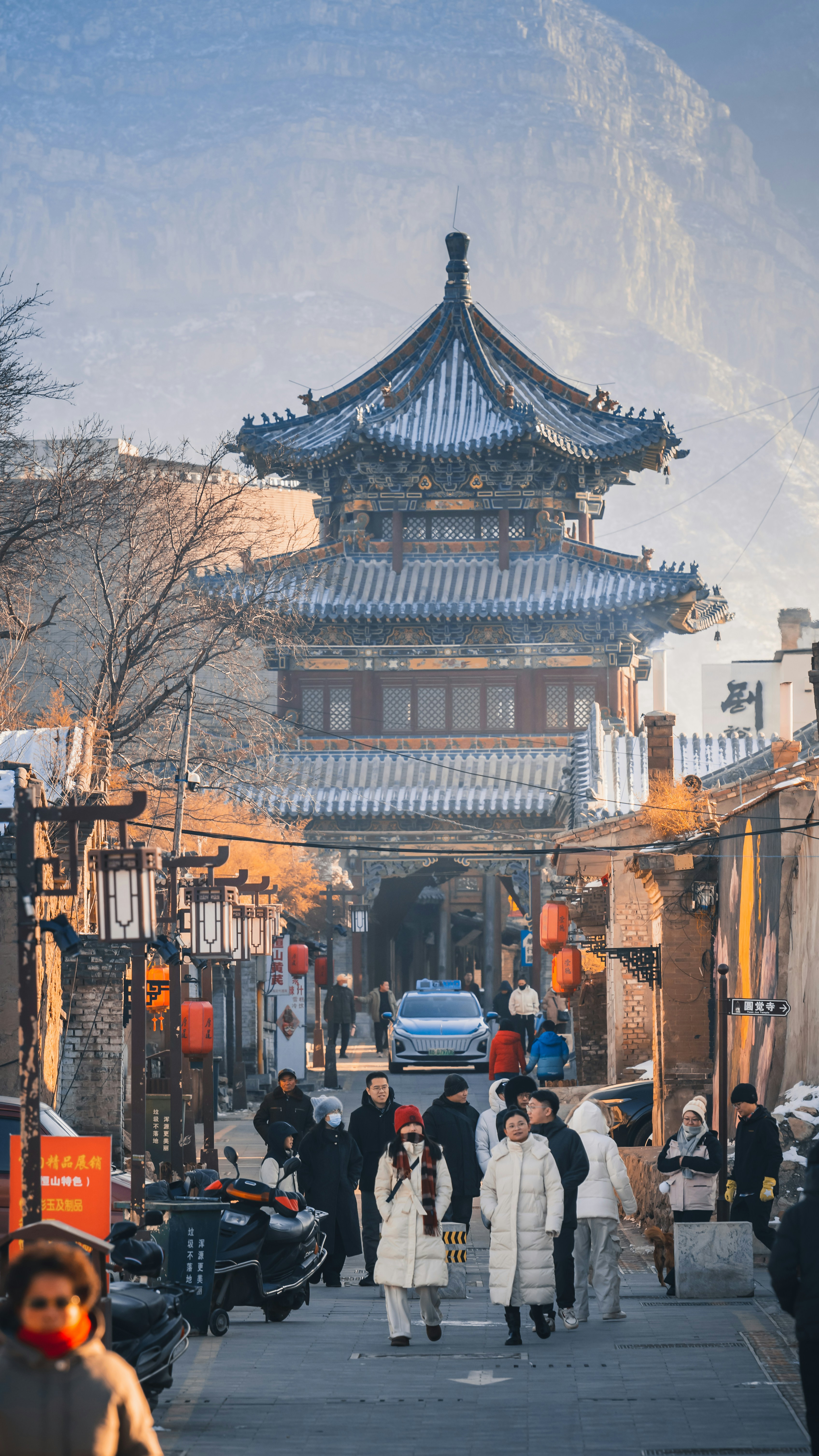 People walk down a street towards an ancient chinese pagoda.