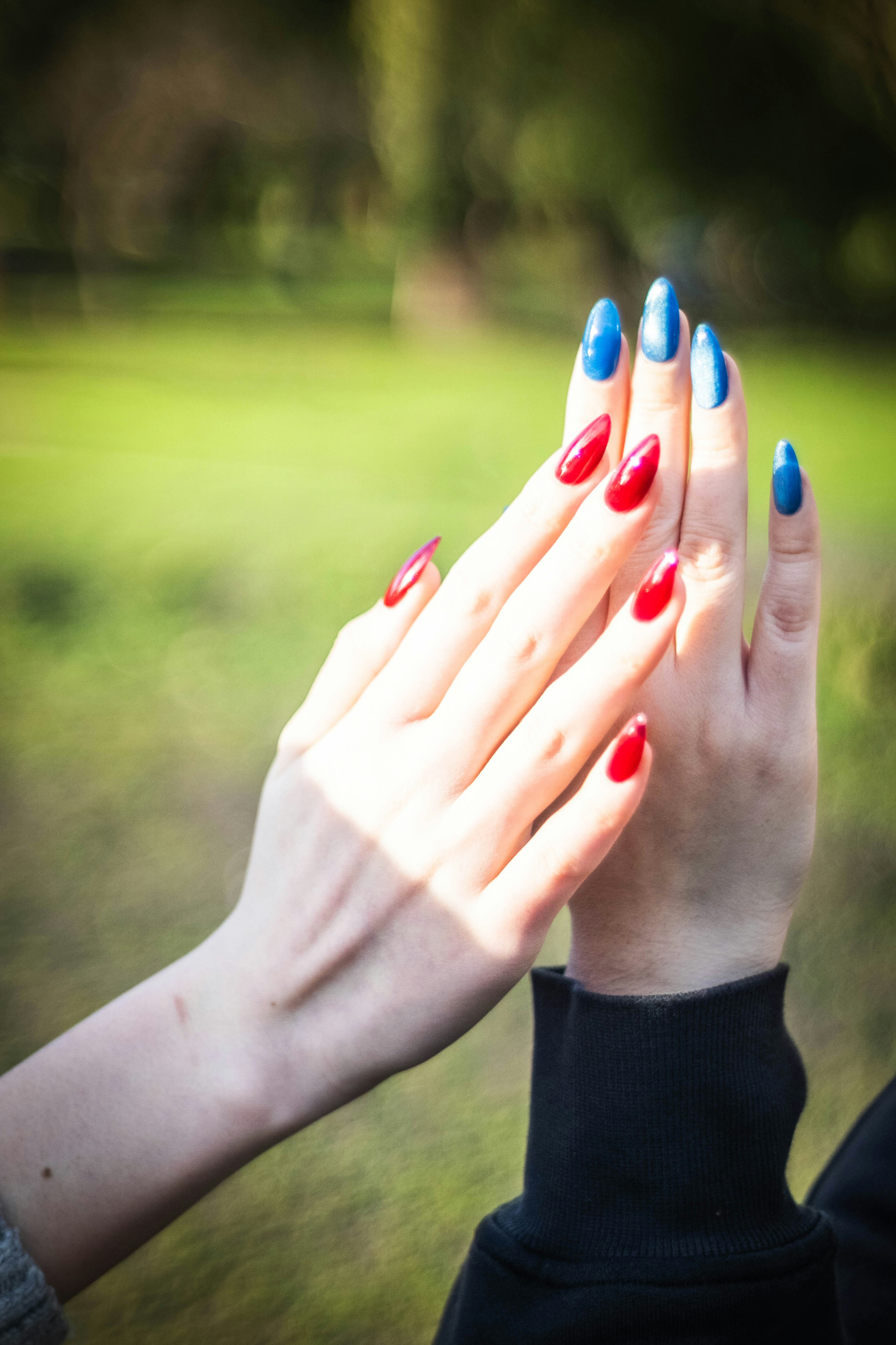Two hands with red and blue painted nails high-fiving.