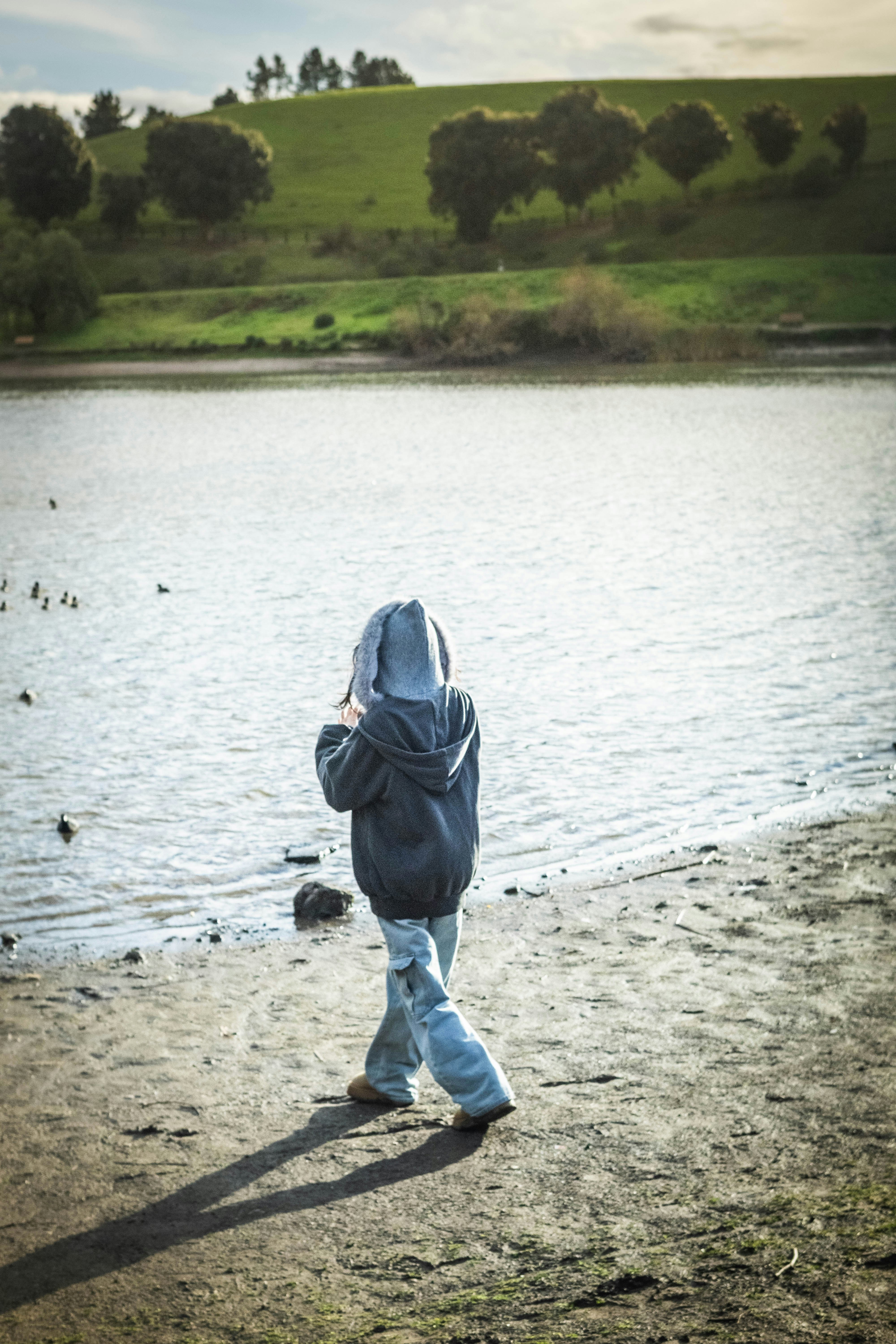 Child in hoodie walks by a lake