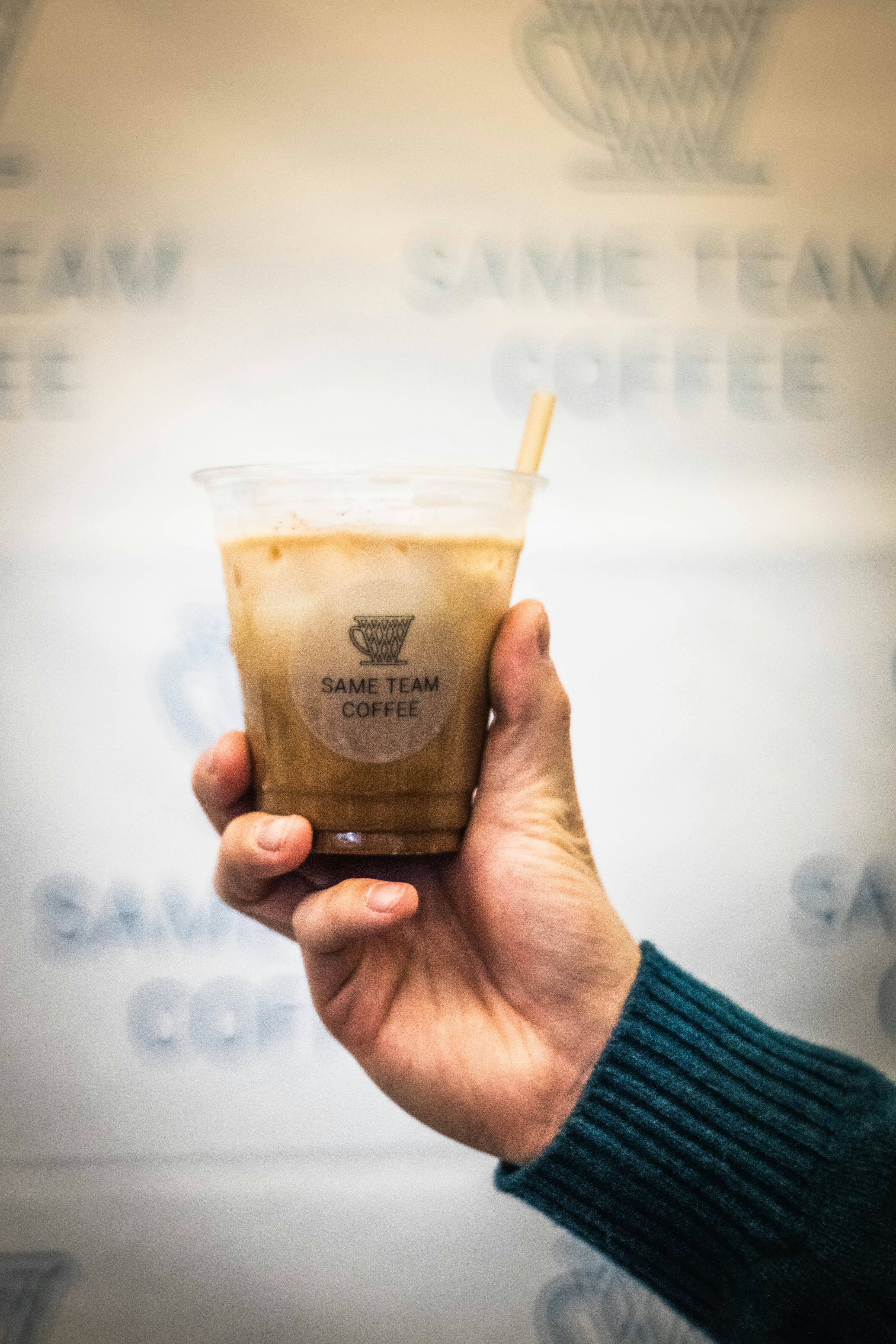 Hand holding a cold coffee drink with straw.