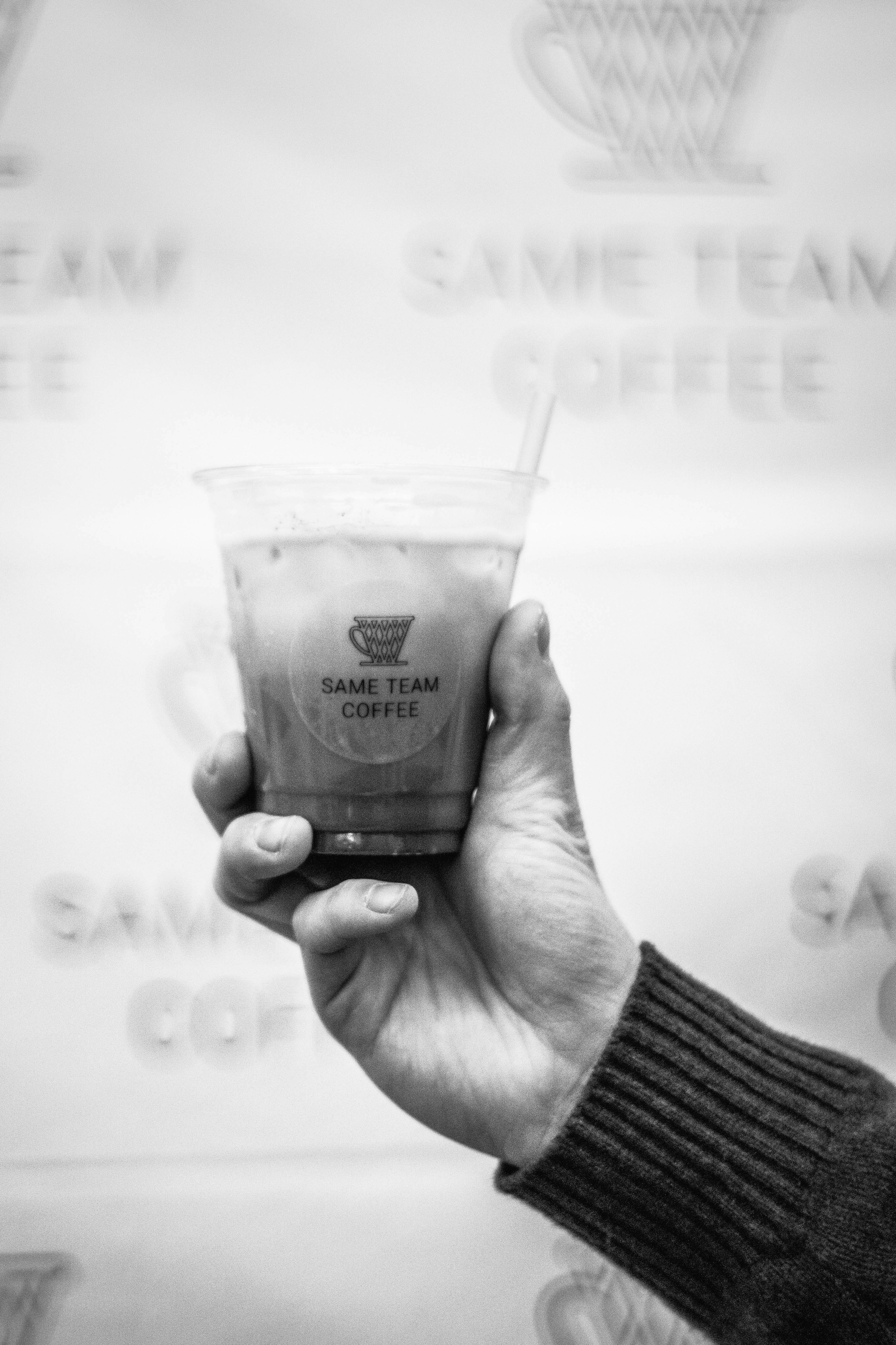 Hand holding a cold coffee drink with logo.
