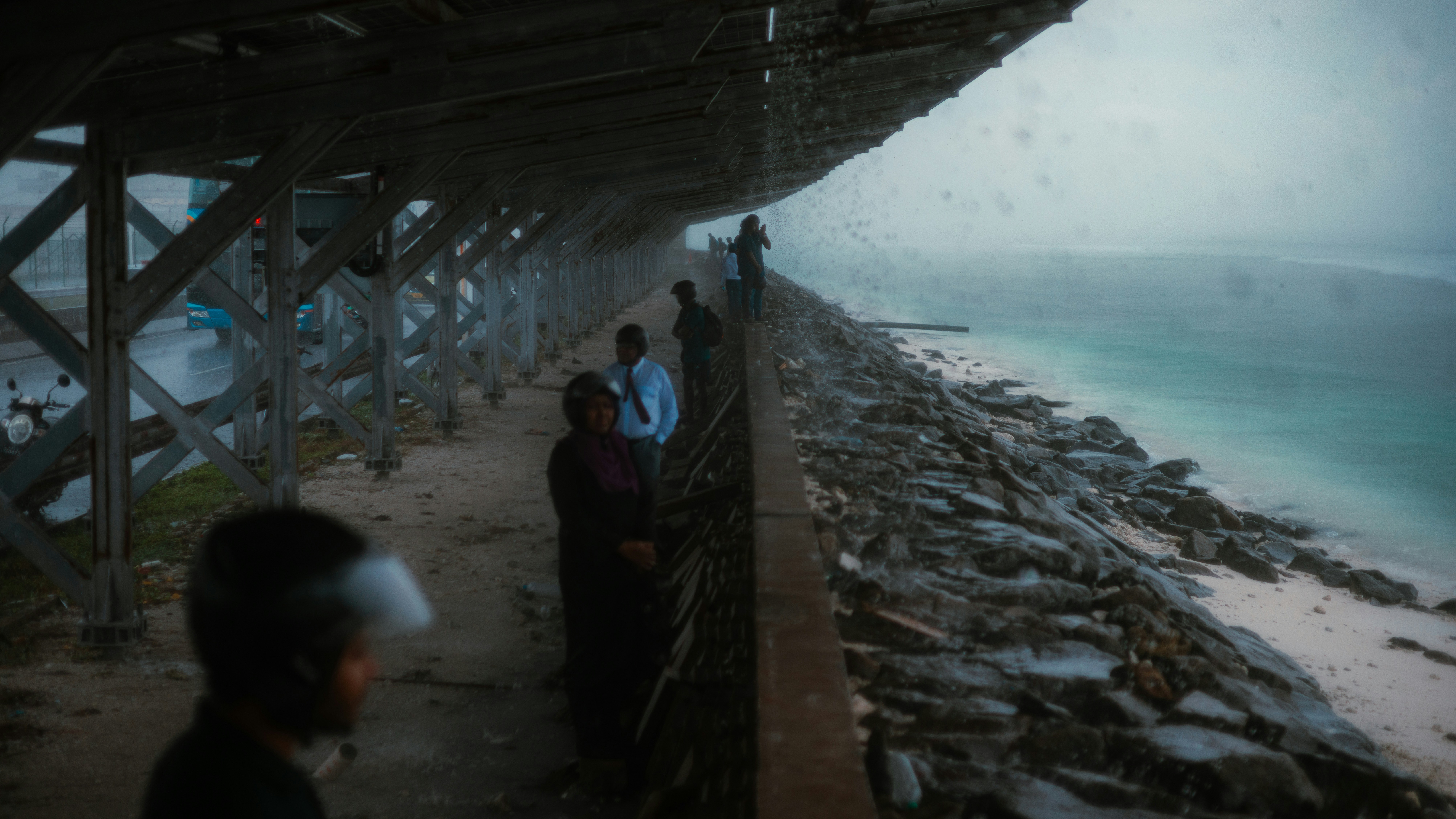People walk along a rocky shore under a structure
