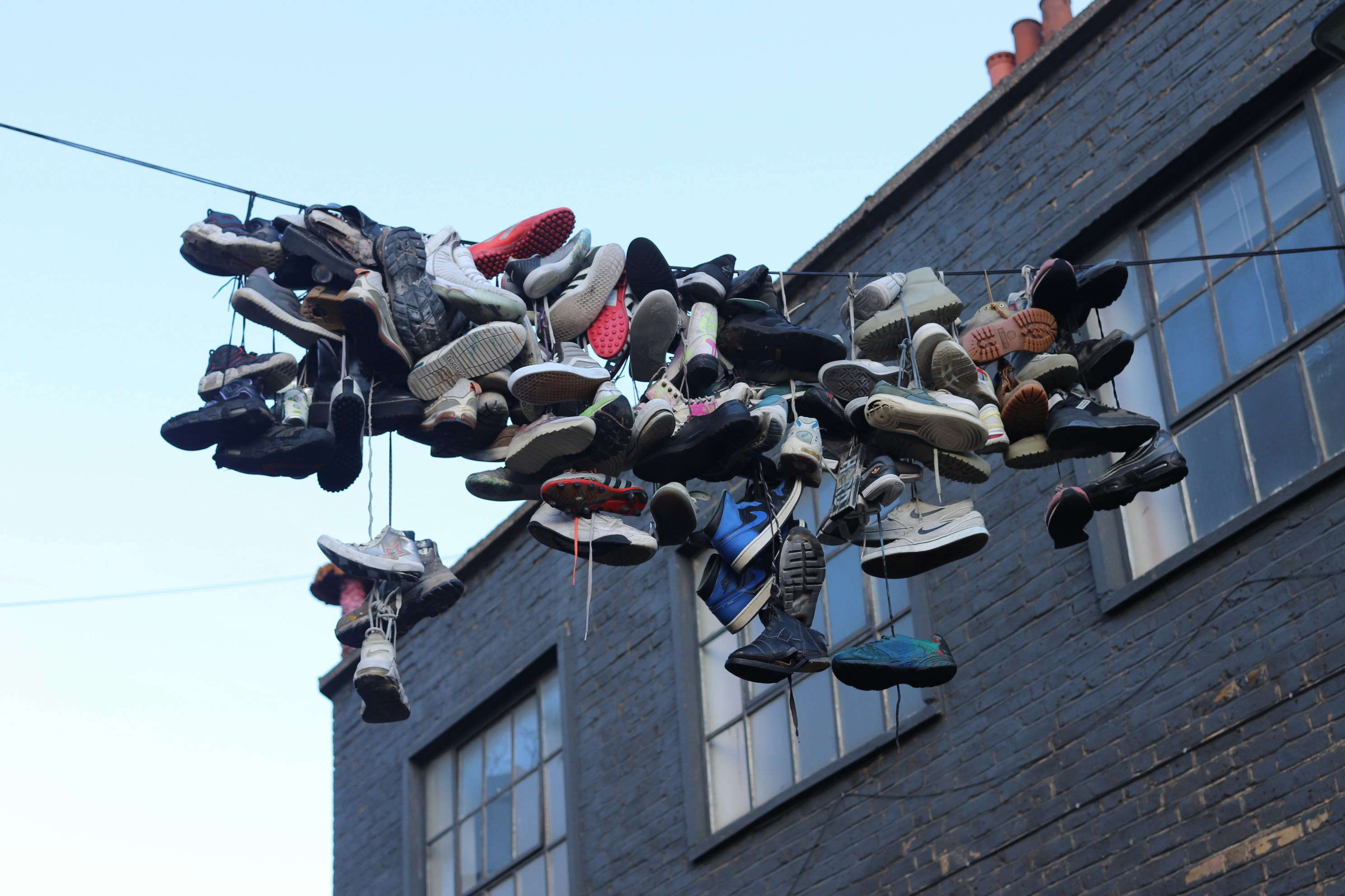 Many shoes hanging on a wire outside building