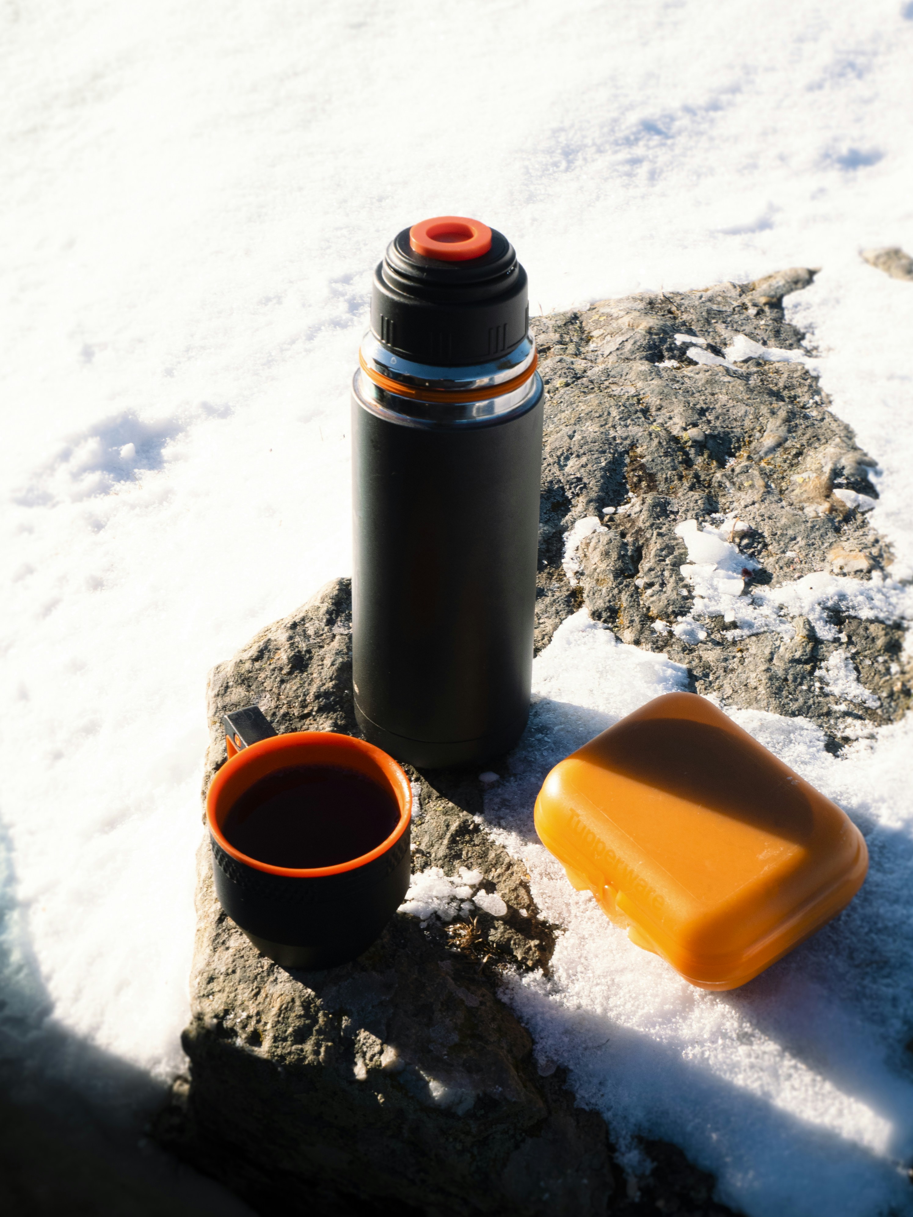 Thermos, cup of coffee, and snack on snow-covered rock.