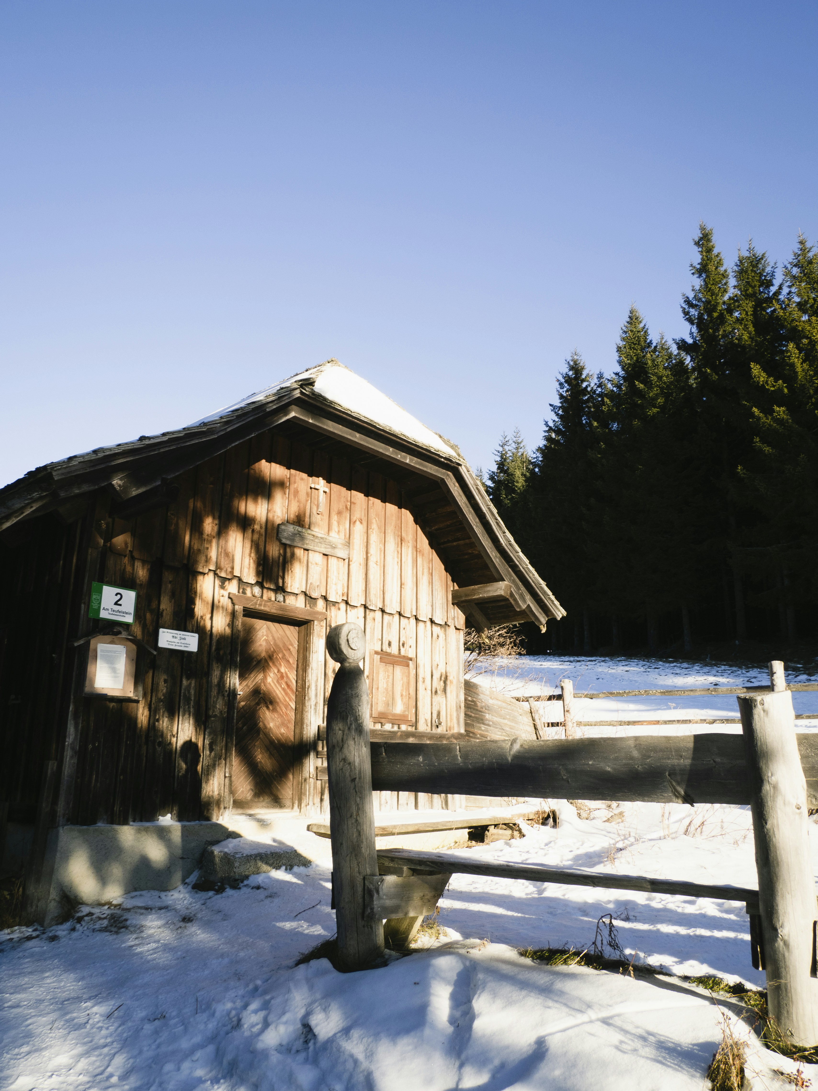 Wooden cabin in a snowy forest with a fence.