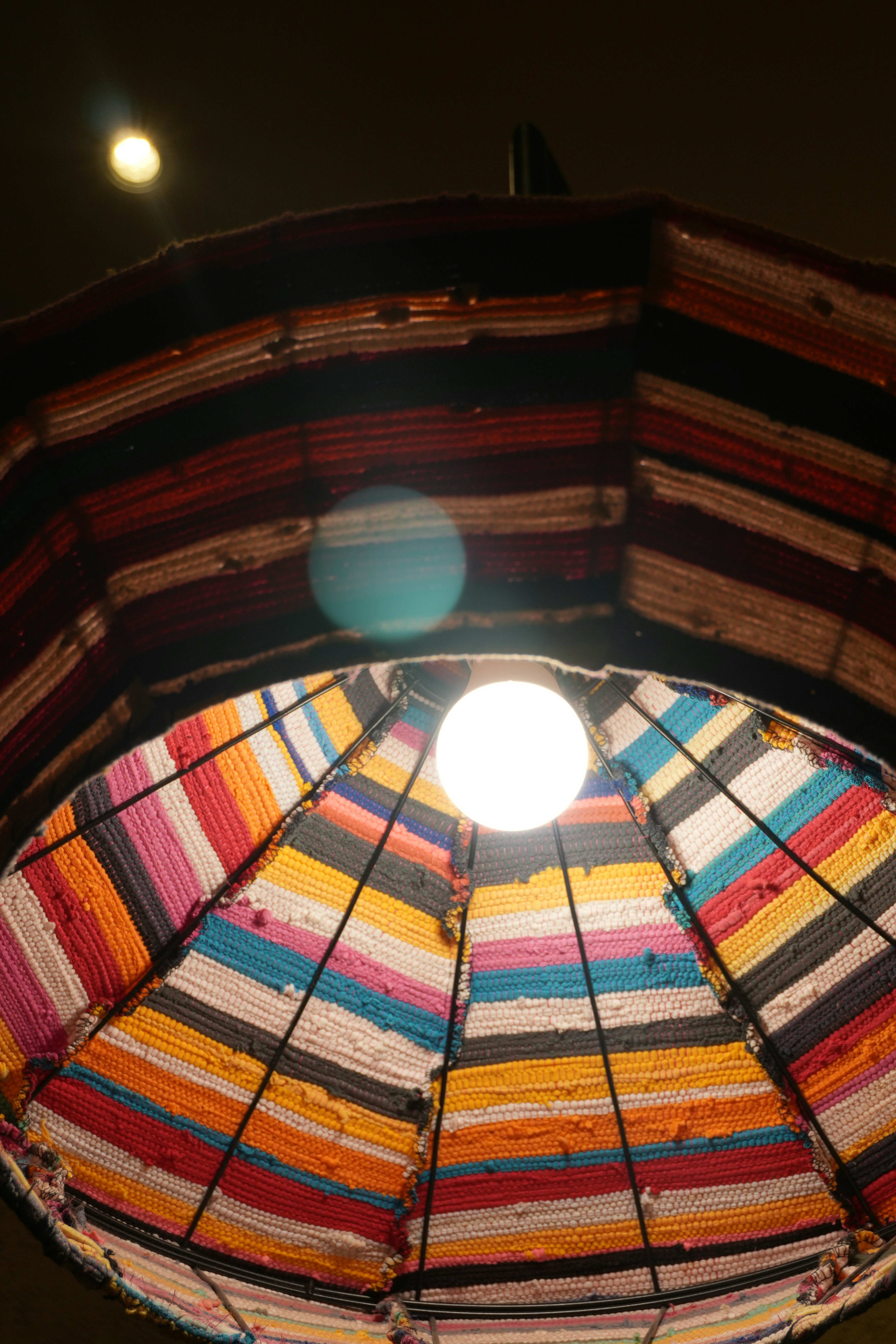 Colorful woven lampshade with a light bulb inside.