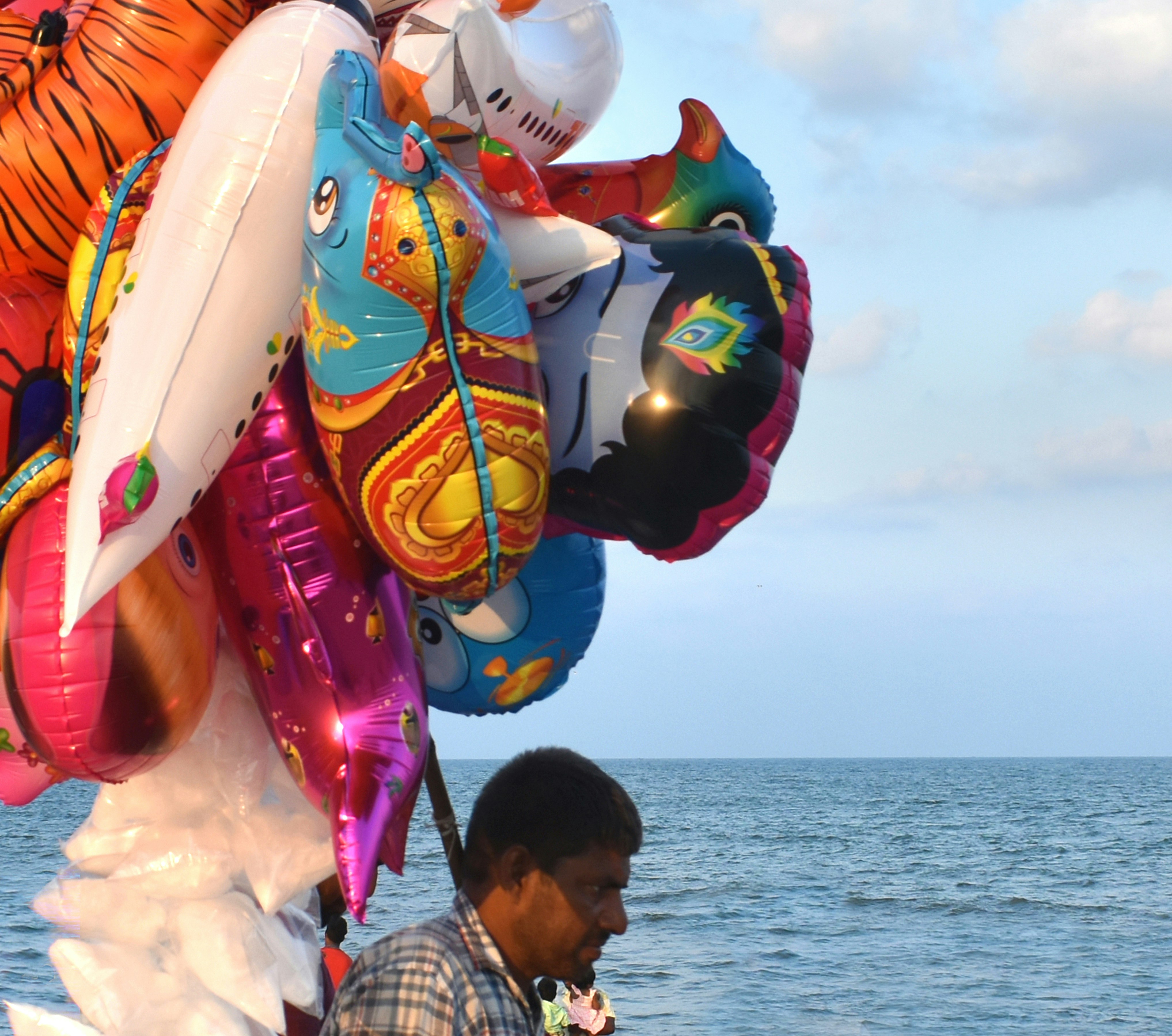 Man holding colorful balloons by the ocean