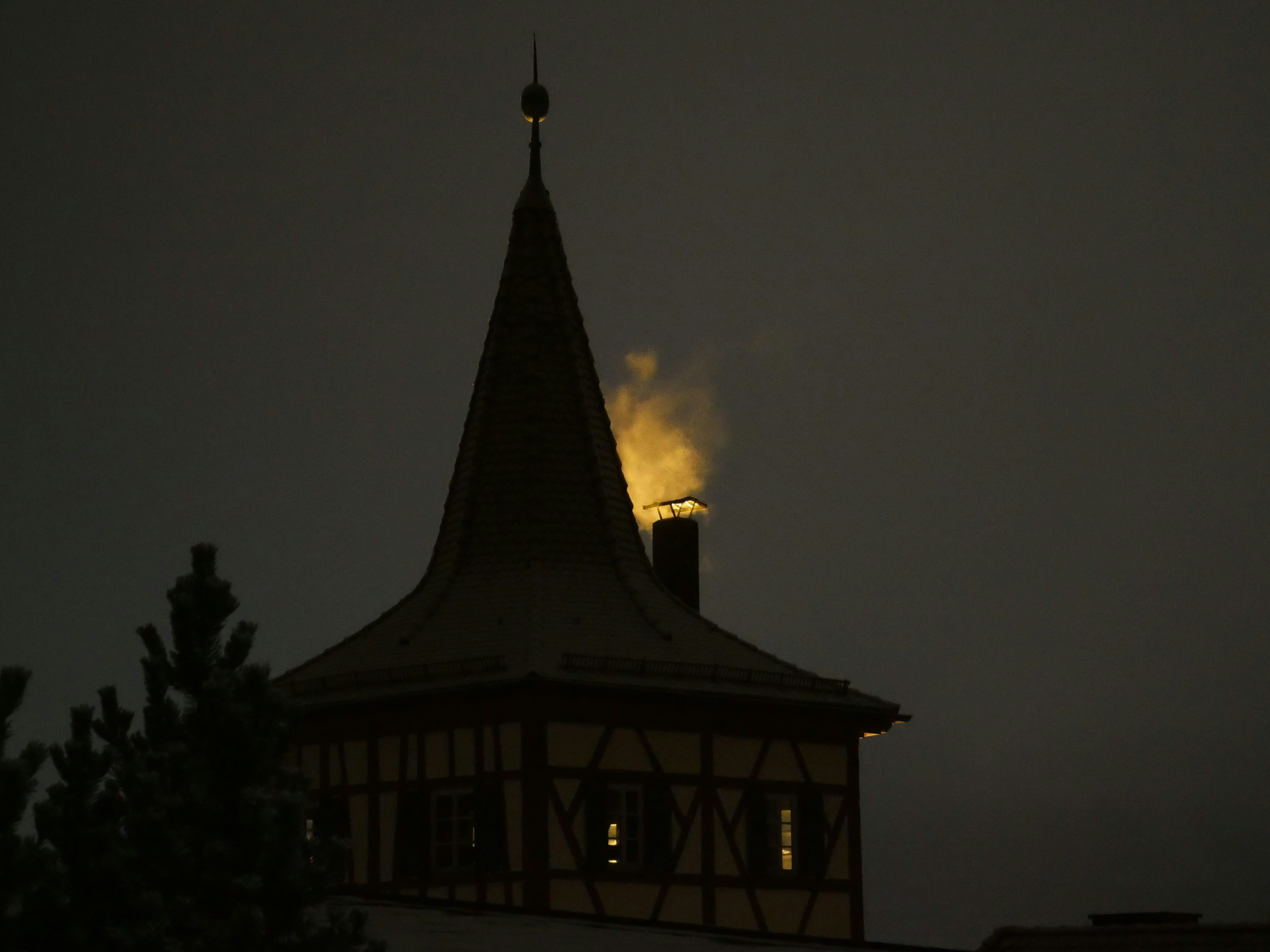 Rauch steigt aus einem Schornstein auf einem dunklen Turm auf.