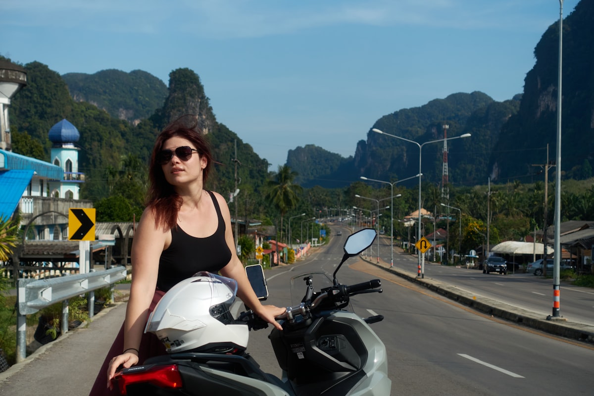 Woman with motorcycle on road with mountains