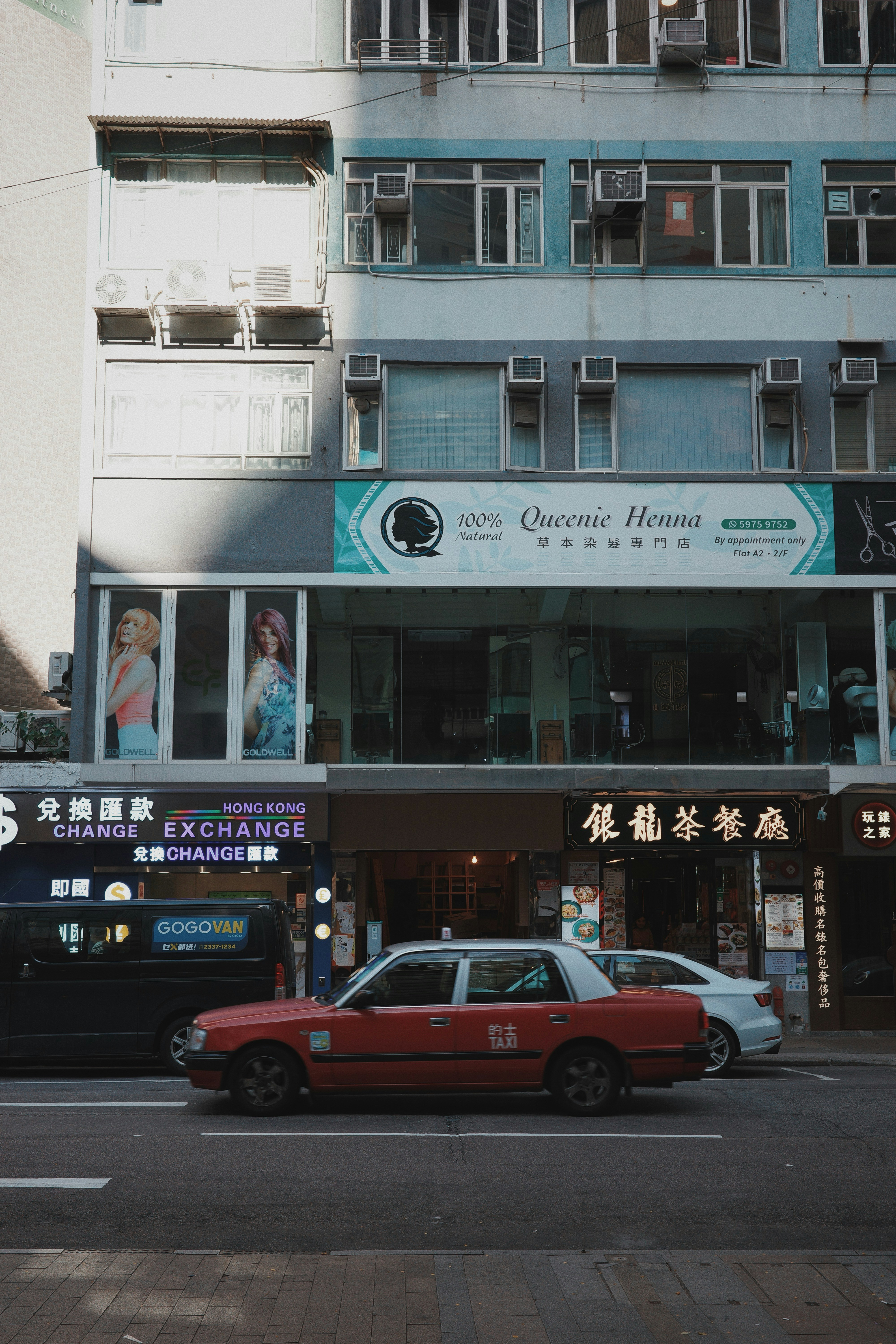 Red taxi drives past storefronts on city street