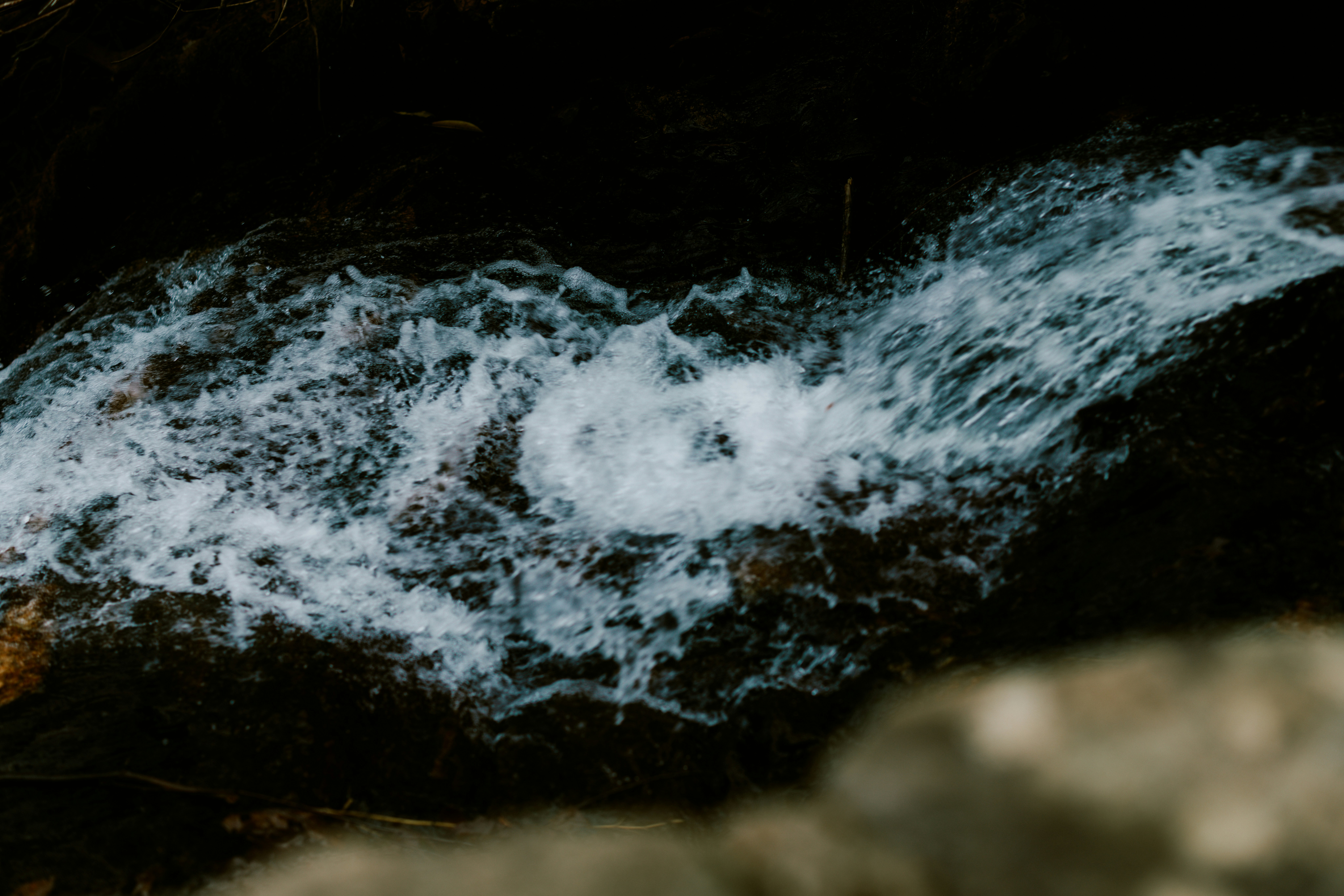 White water cascades over dark rocks in a stream.