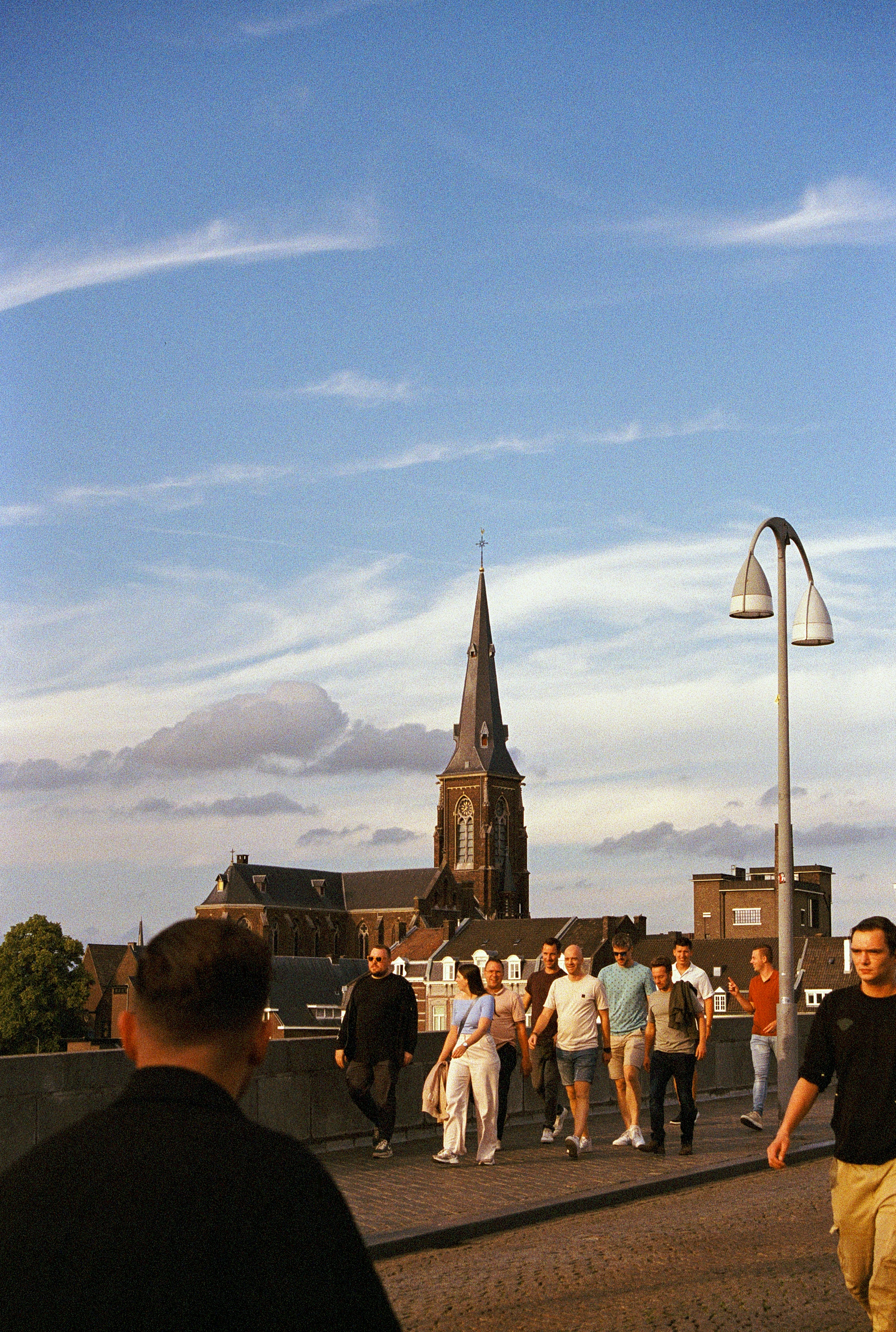 People walk across a bridge with a church spire.