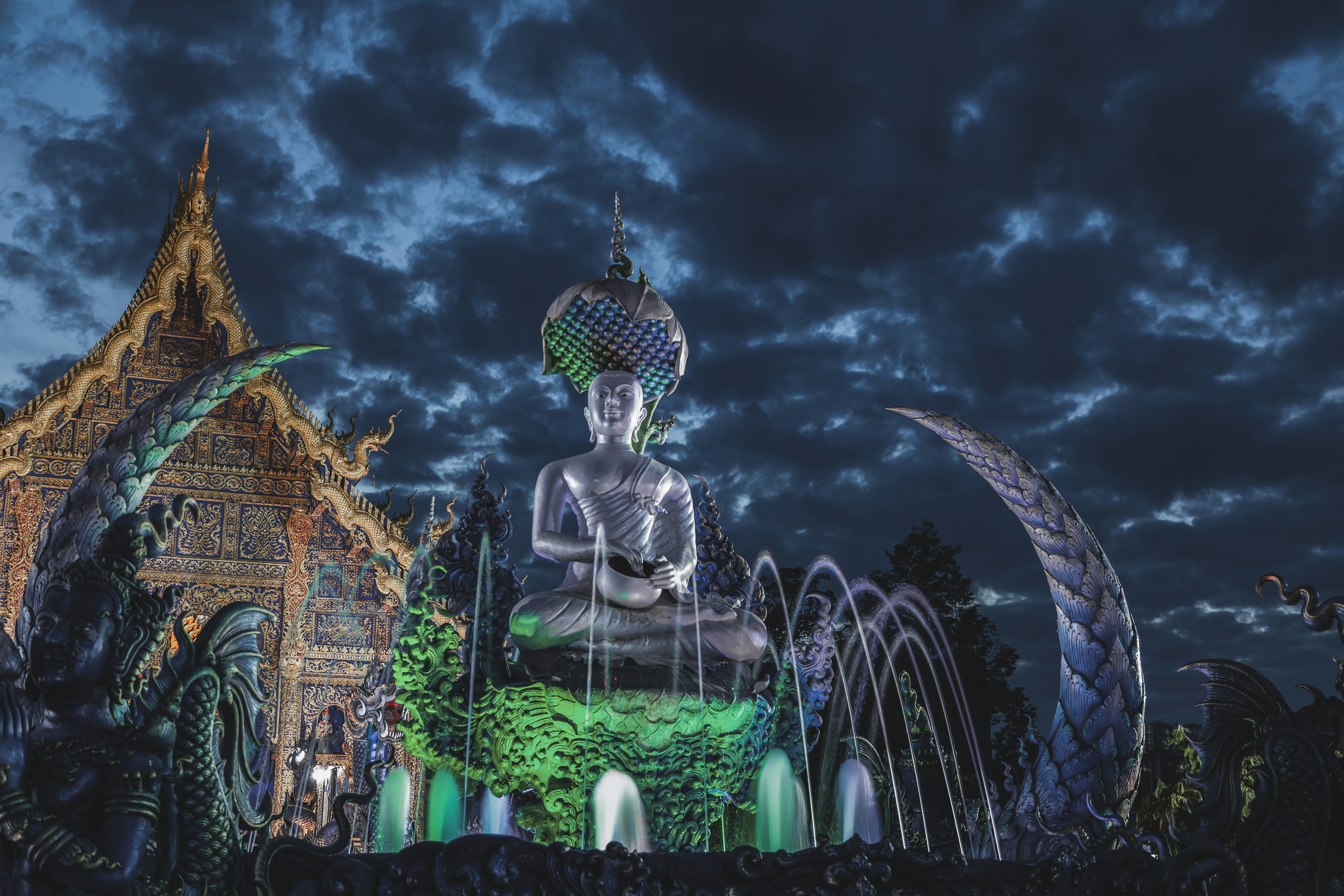 A large buddha statue illuminated at night with fountains