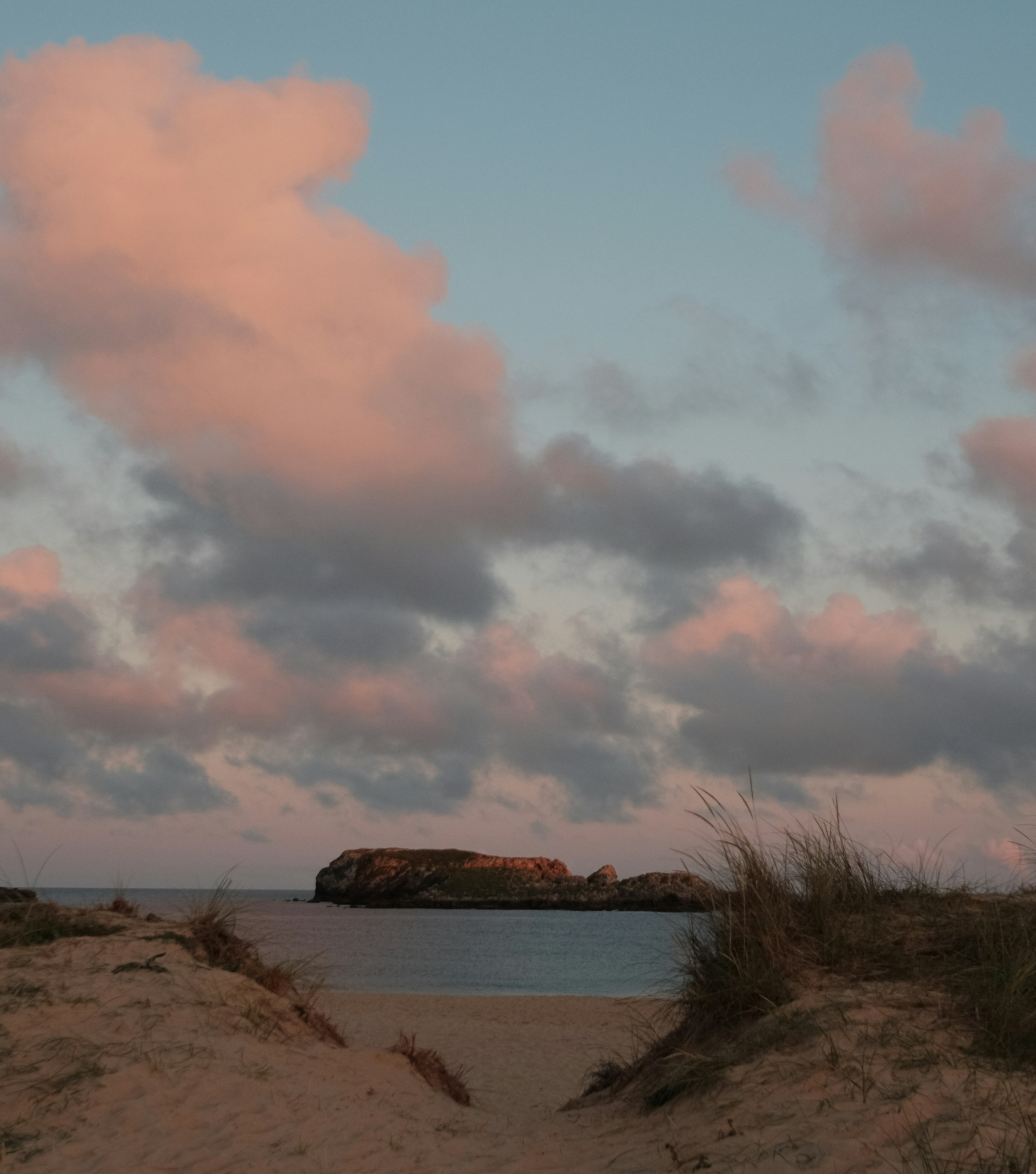 Rosa Wolken über einer fernen Insel bei Einbruch der Dämmerung