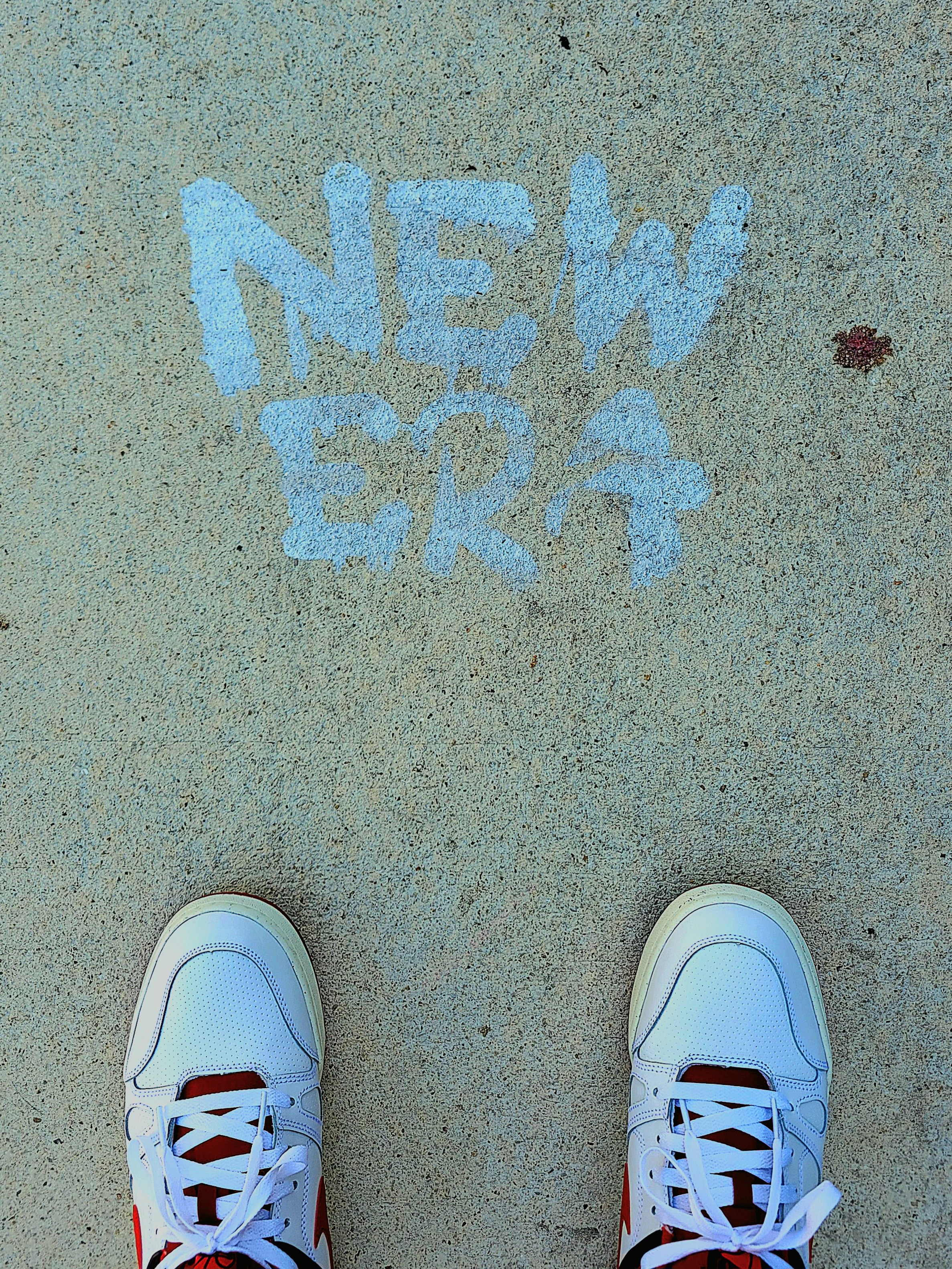 White sneakers stand before 'new era' chalked on pavement.