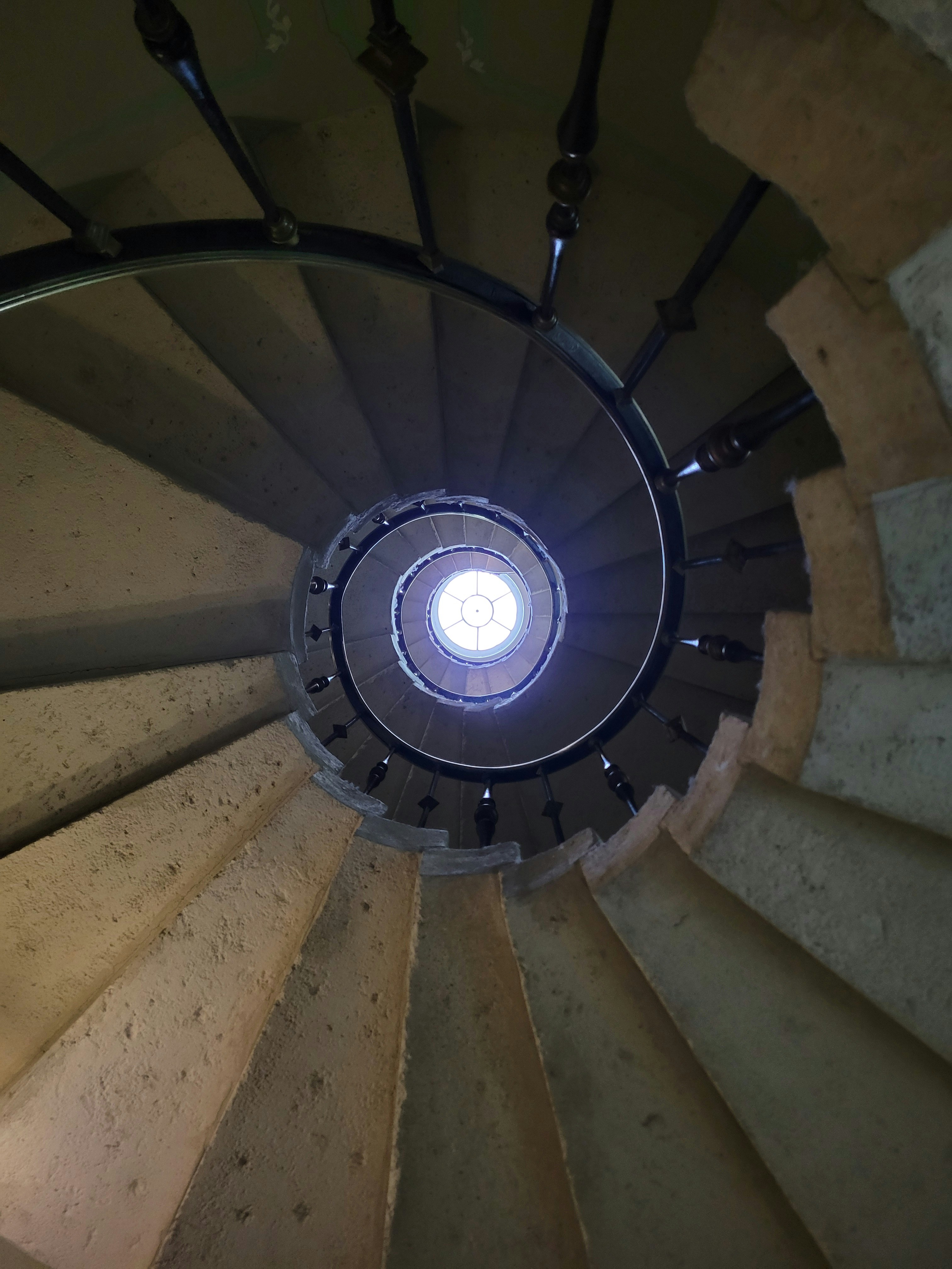Looking up a spiral staircase towards a skylight.