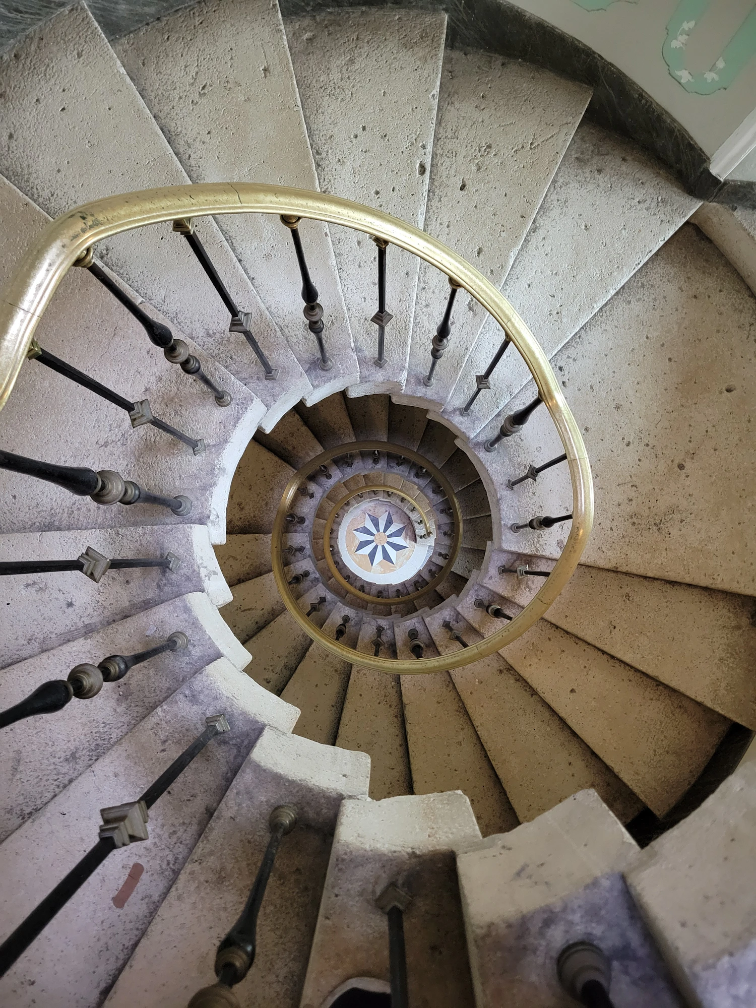 A stone spiral staircase photographed from above, its brass handrail curling inward